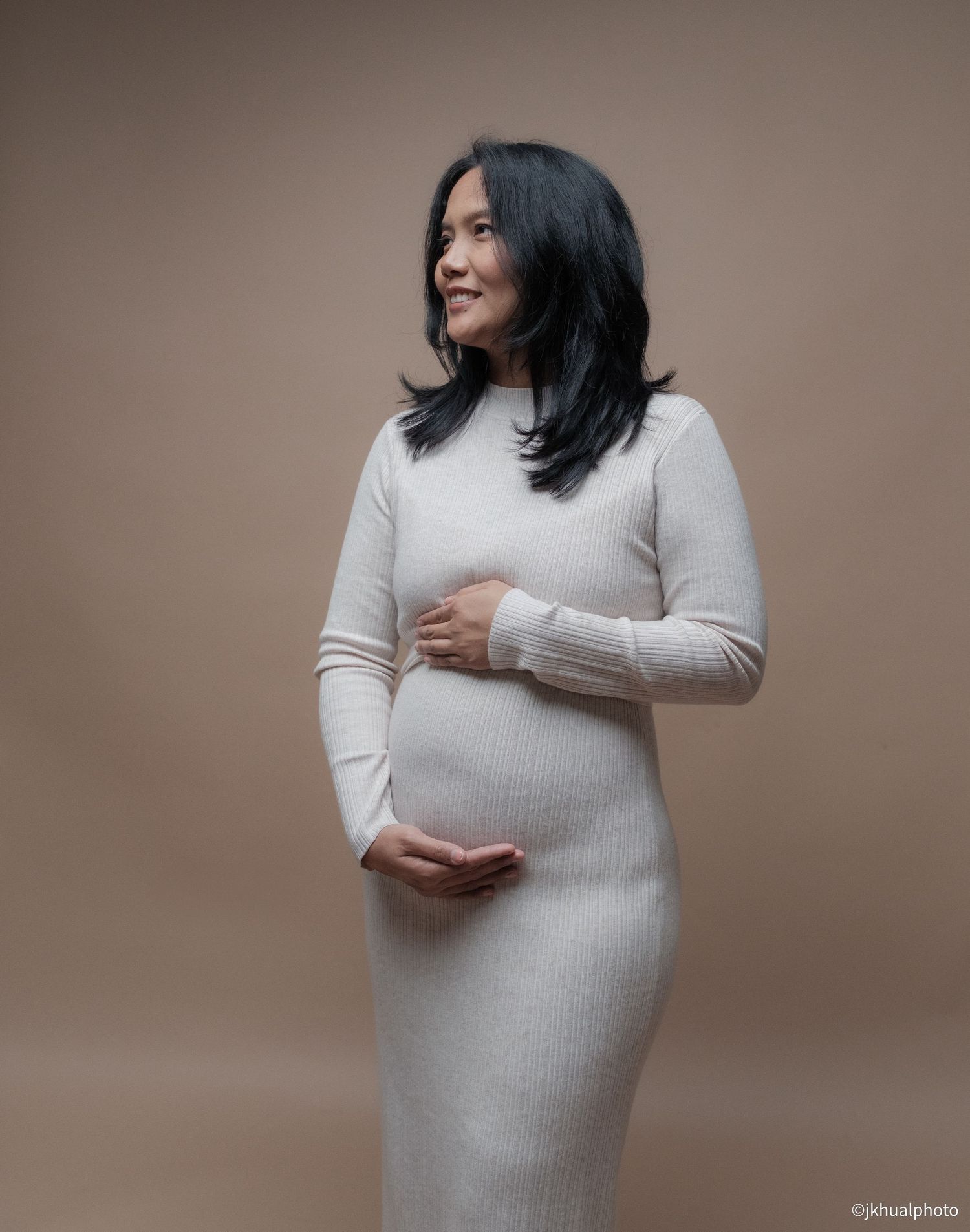 A series of maternity photos showing a woman in a white sweater dress posing against a neutral beige backdrop.