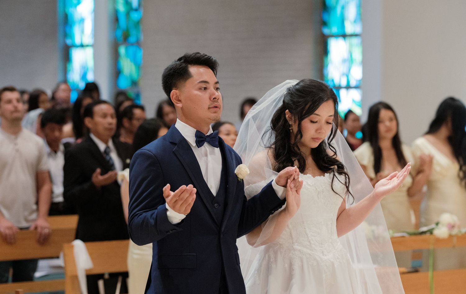 A couple worships together during their wedding ceremony in a church with stained glass windows.