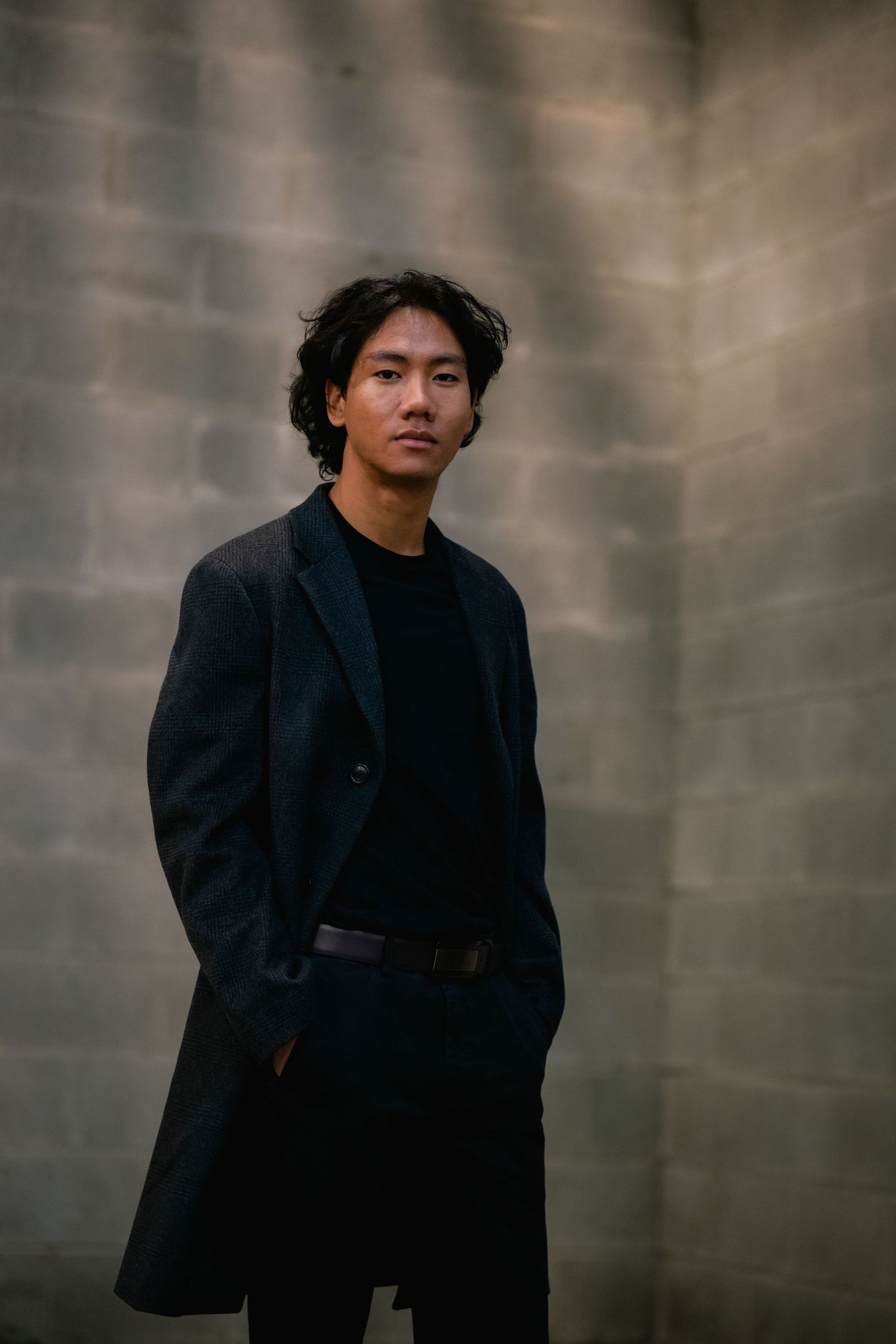 Person wearing all black creates artistic poses against concrete backdrop.