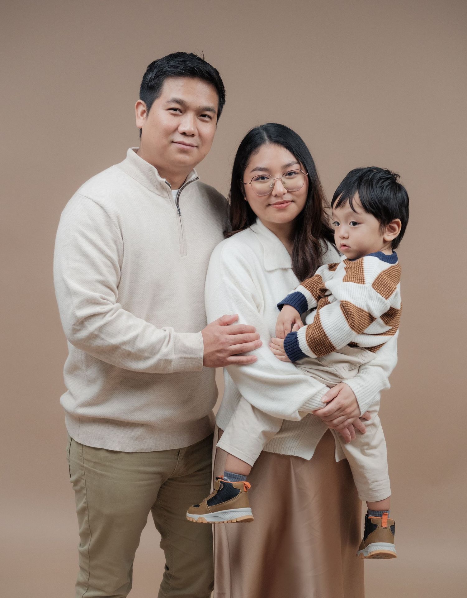 Studio portraits of a family in cream-colored outfits showing playful interactions.