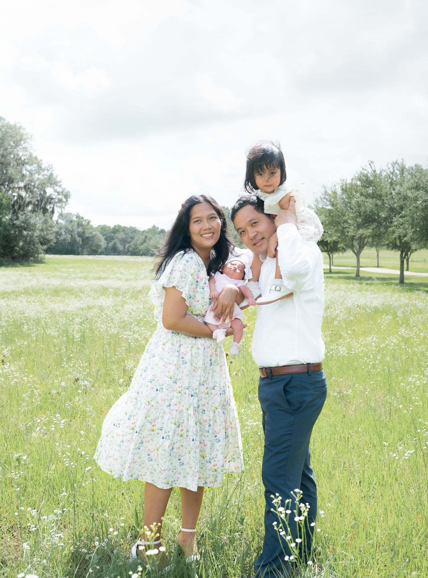 Happy family of four poses in a wildflower meadow with two young children on a cloudy day.