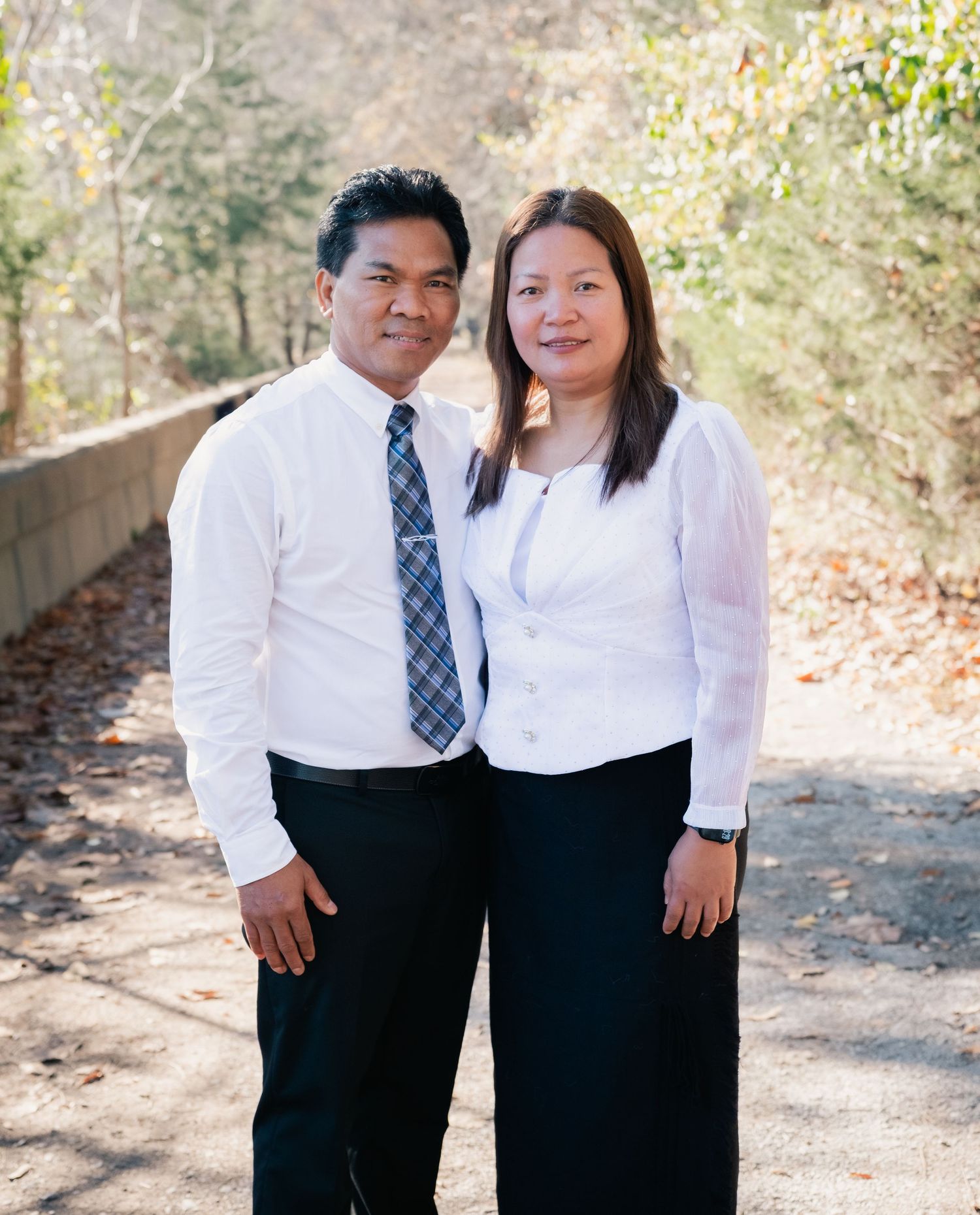 A couple shares a tender moment while posing in matching formal wear on a wooded path.