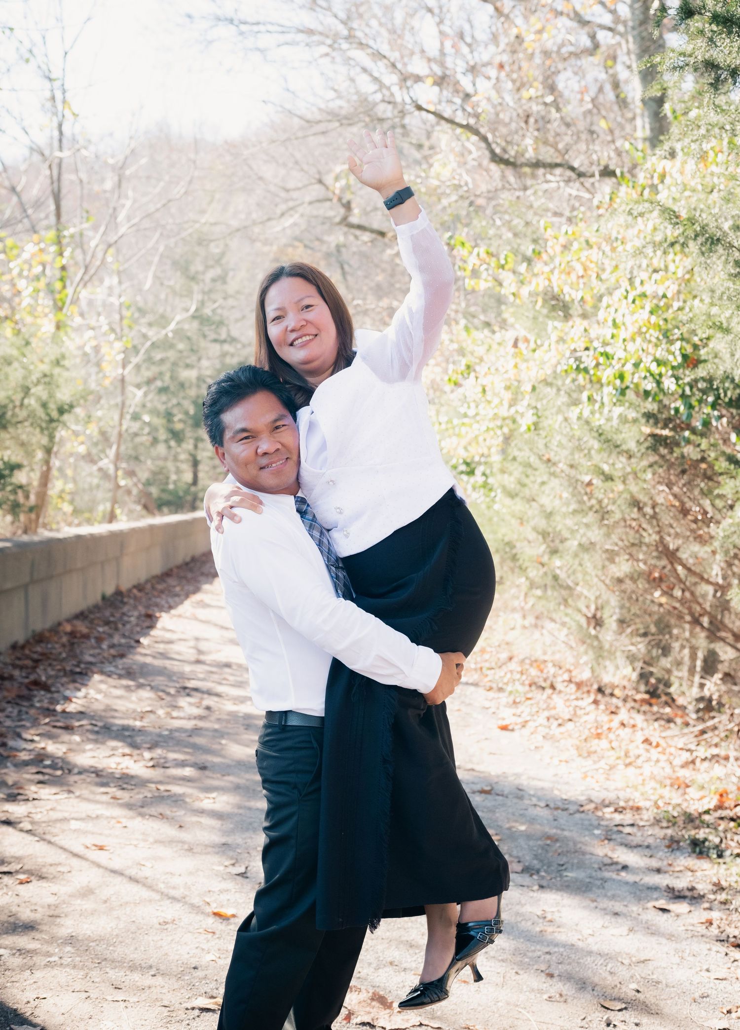 A playful couple in formal wear shares a romantic dance pose on a wooded trail.