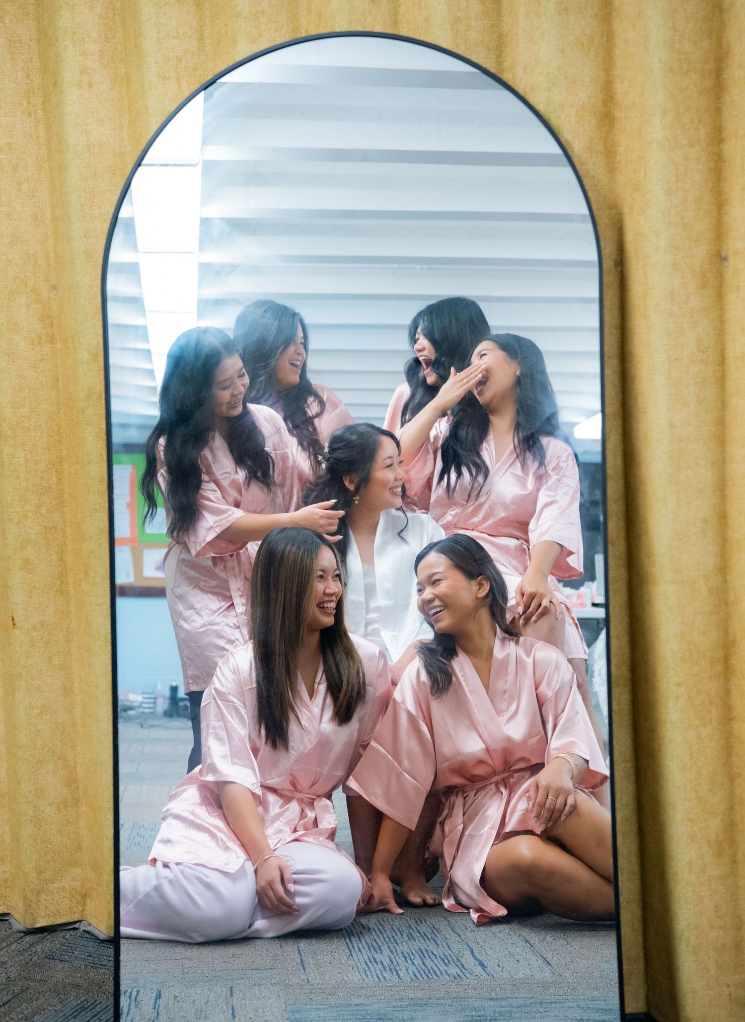 Group wearing matching pink silk robes lounging on floor during pre-wedding preparations.