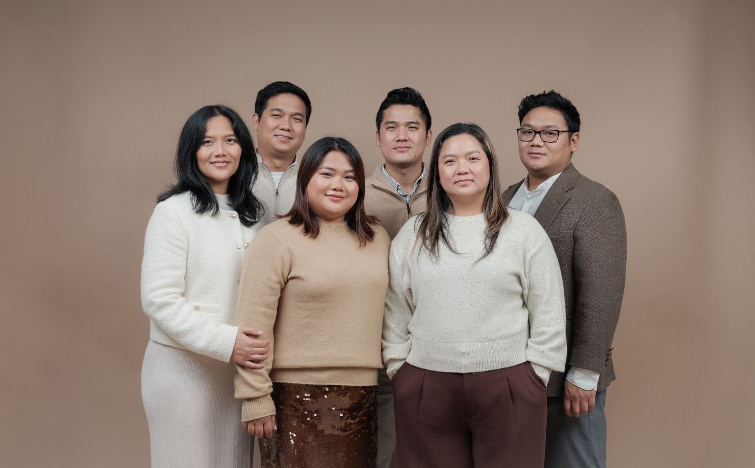 Six people posed together in cream and brown clothing against neutral background.