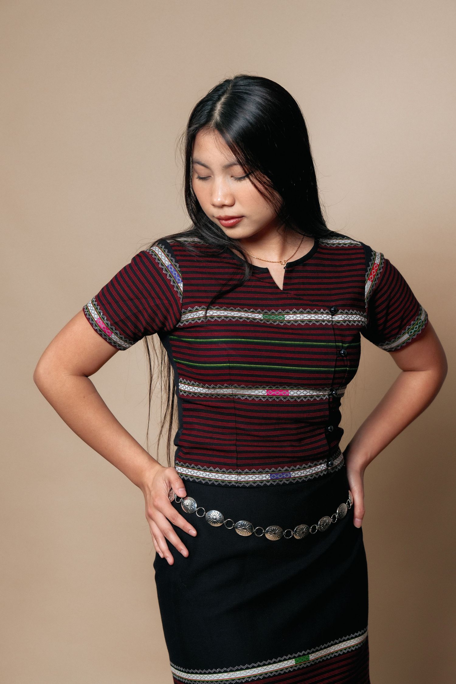Fashion portrait showing details of burgundy striped top with metallic belt and embellishments.