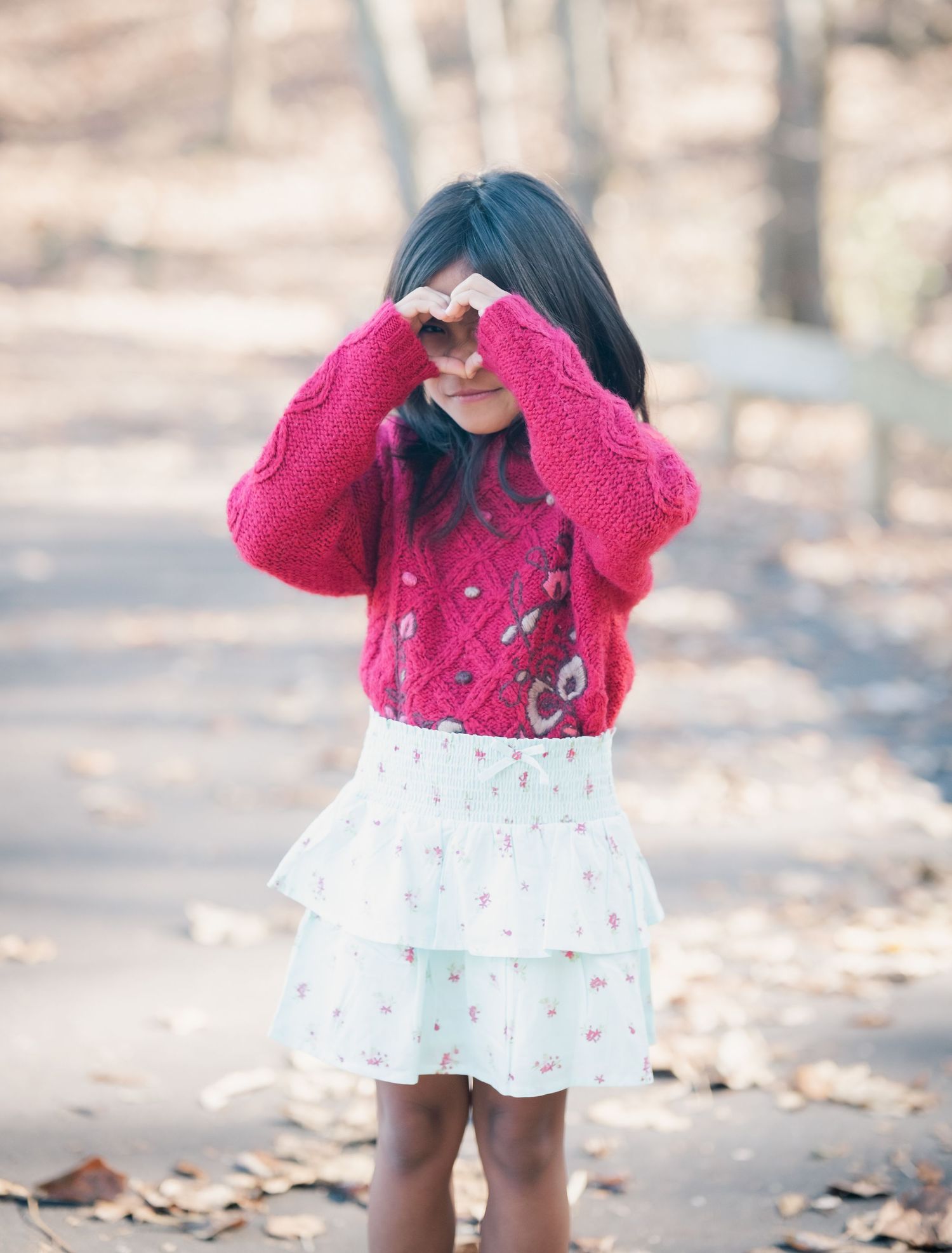 Young person in red sweater and white skirt twirling on forest path.