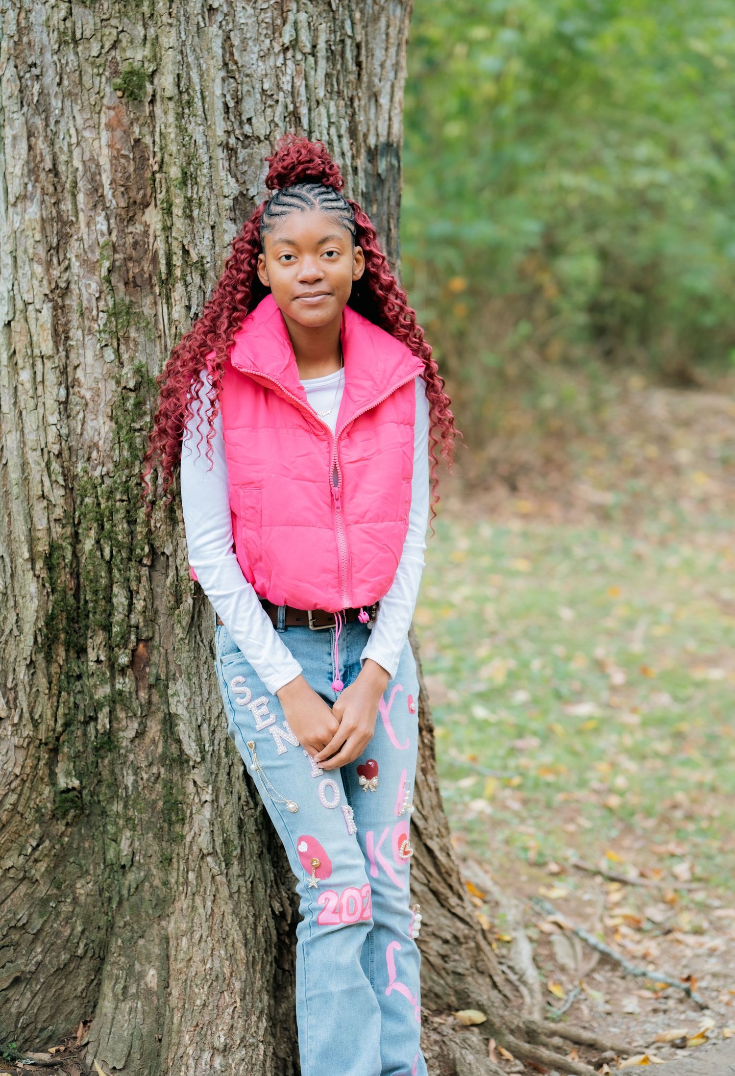 Person in casual attire leaning against large tree trunk in wooded setting.