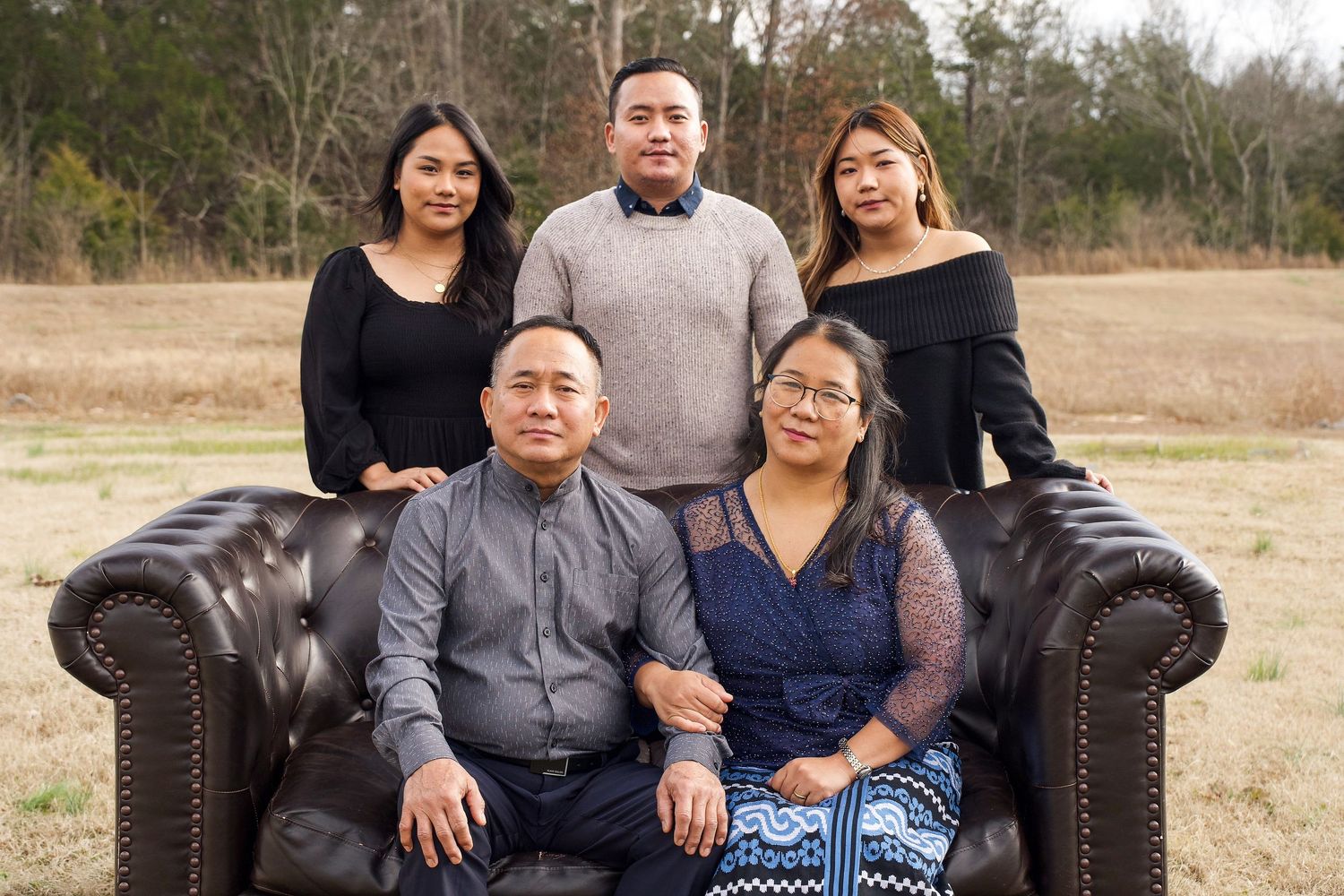 Family portrait session outdoors on leather couch in casual attire.