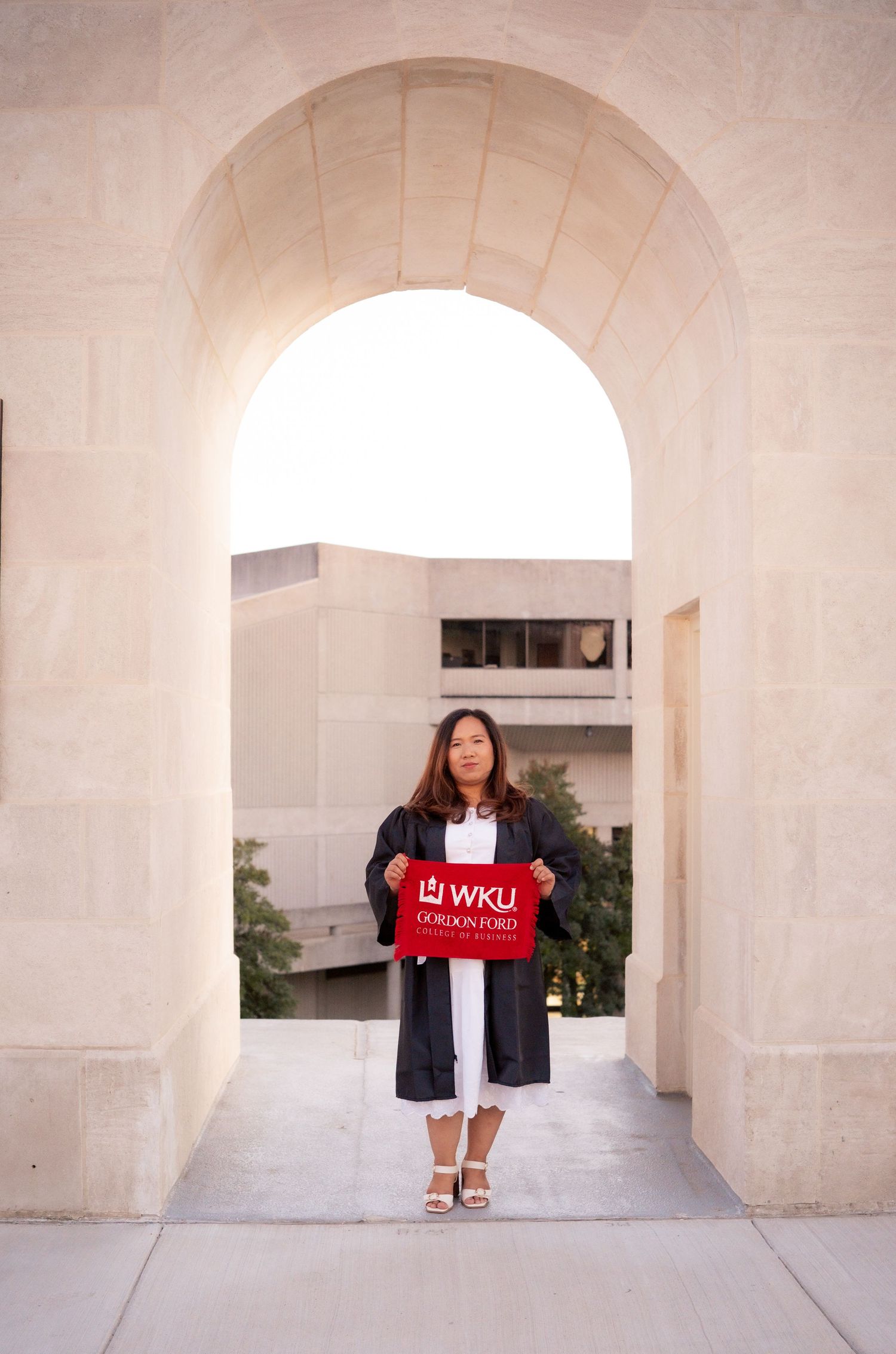 Graduate poses under arched passageway with WKU banner during graduation photoshoot.