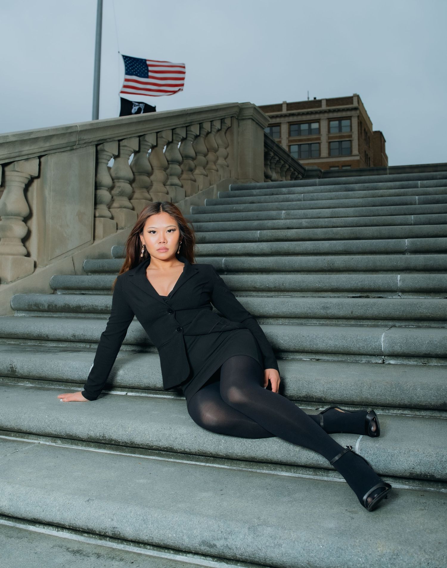 A model in black attire poses on stone steps with an American flag visible in the background.