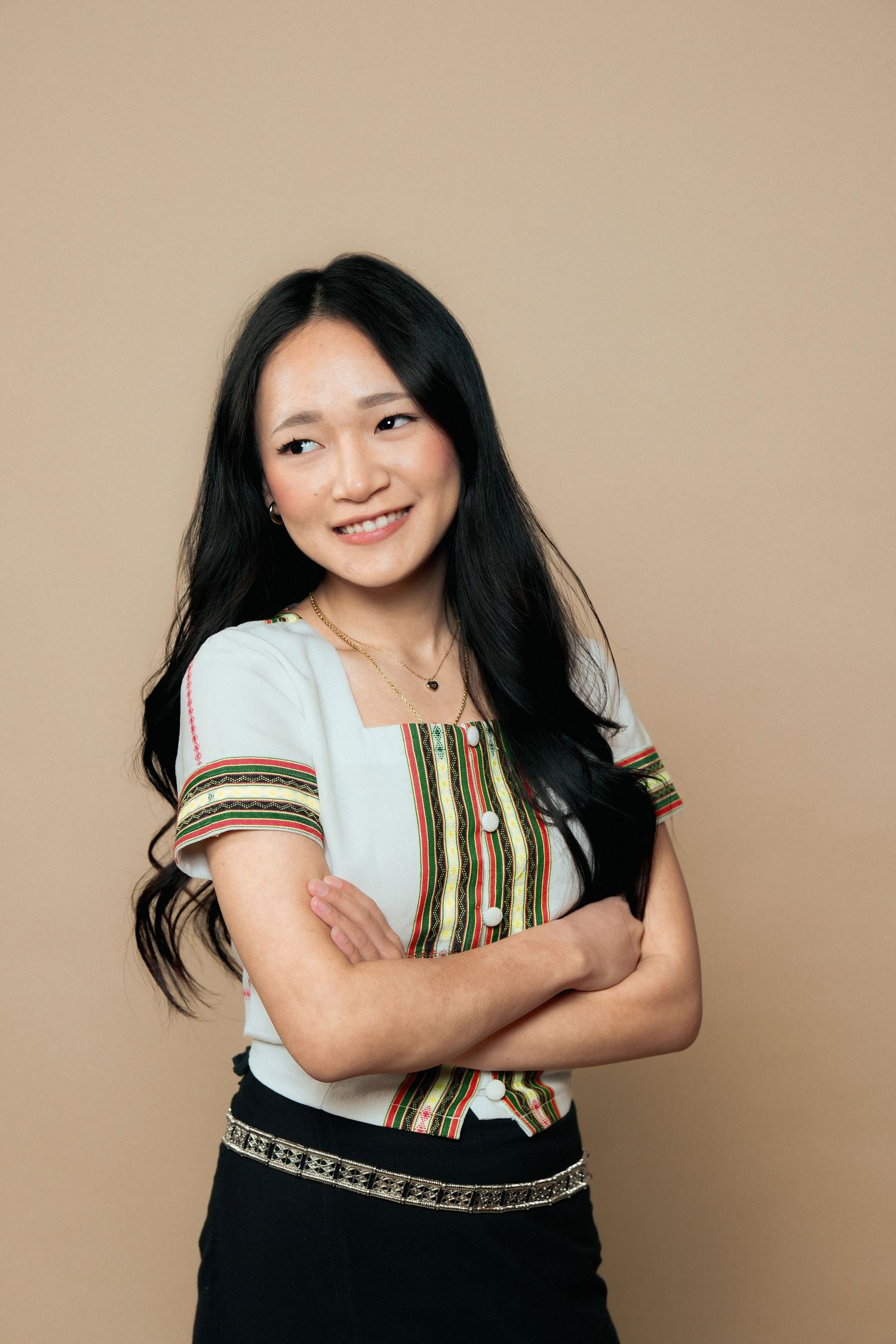 Woman in ethnic attire smiles warmly while posing against neutral backdrop.