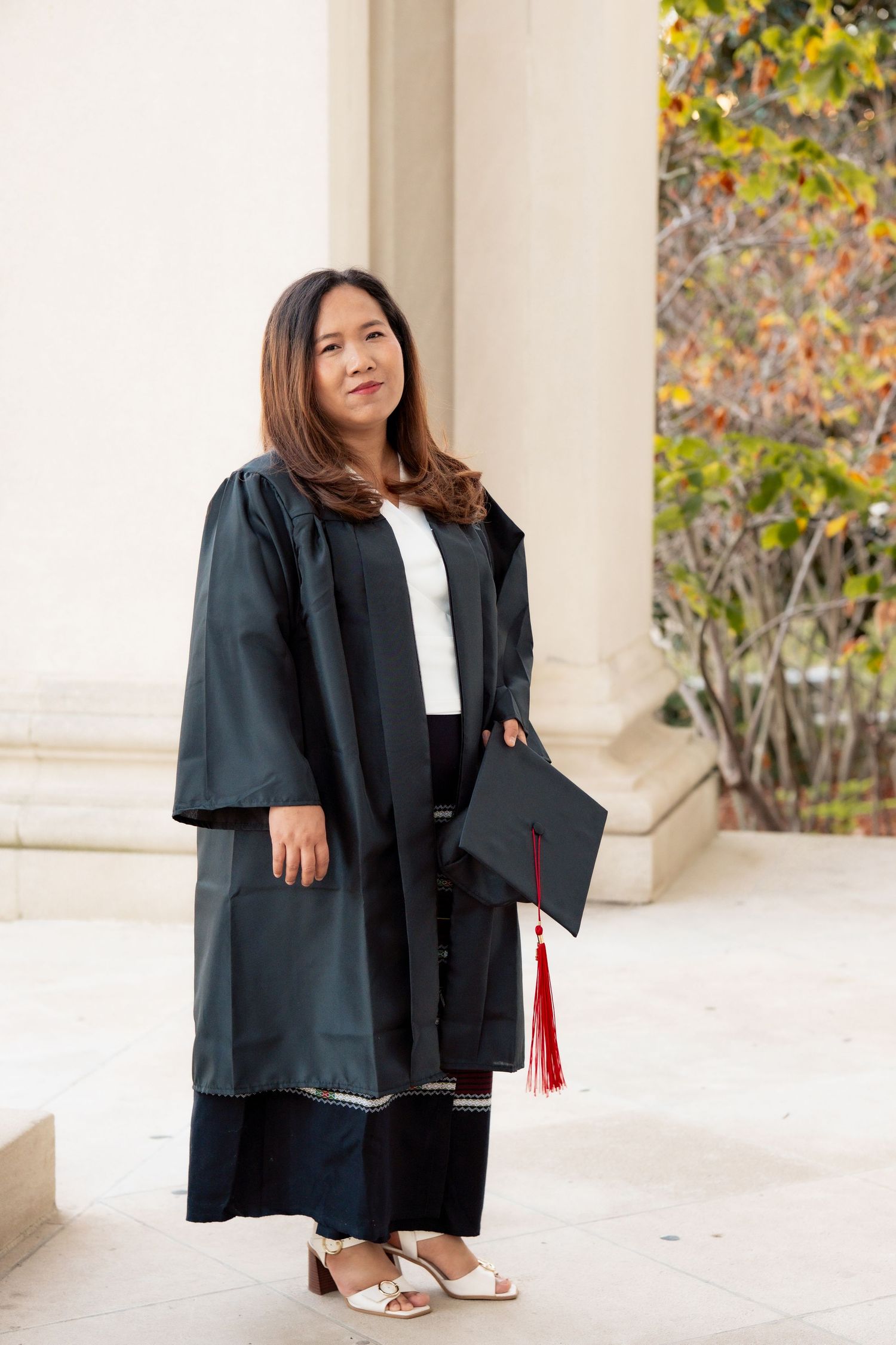 Graduate in black academic regalia poses in front of white columns during graduation photoshoot.