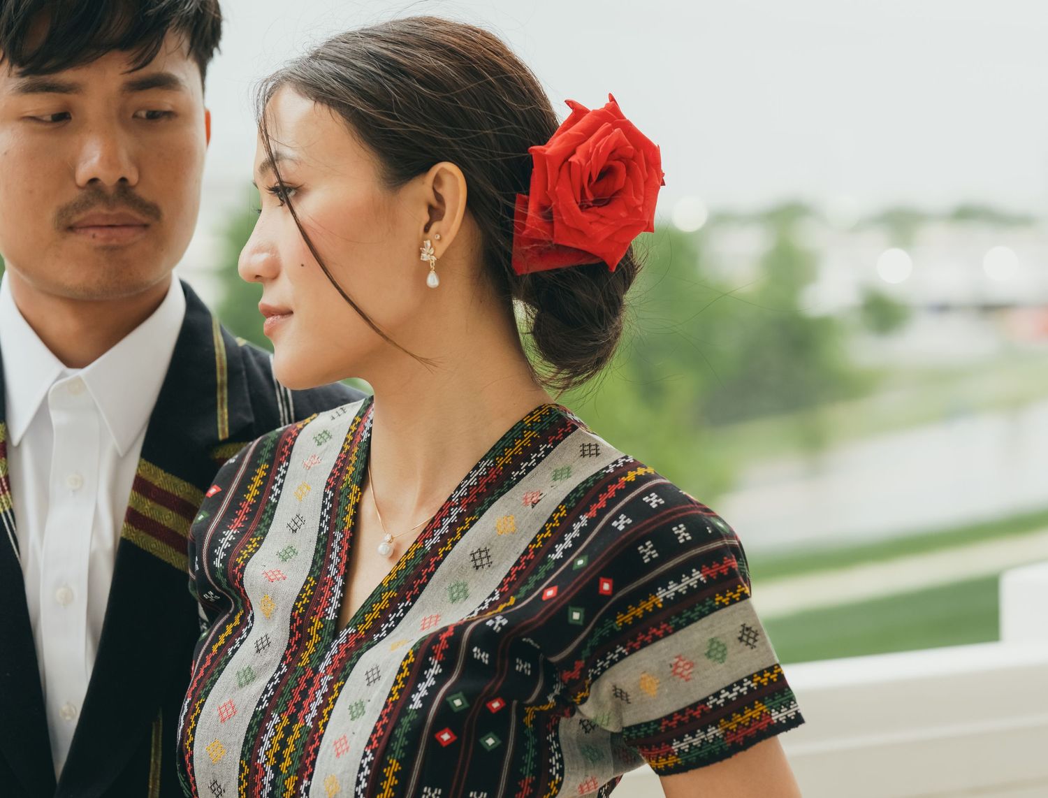 Traditional Hmong couple in cultural dress poses near white columns.