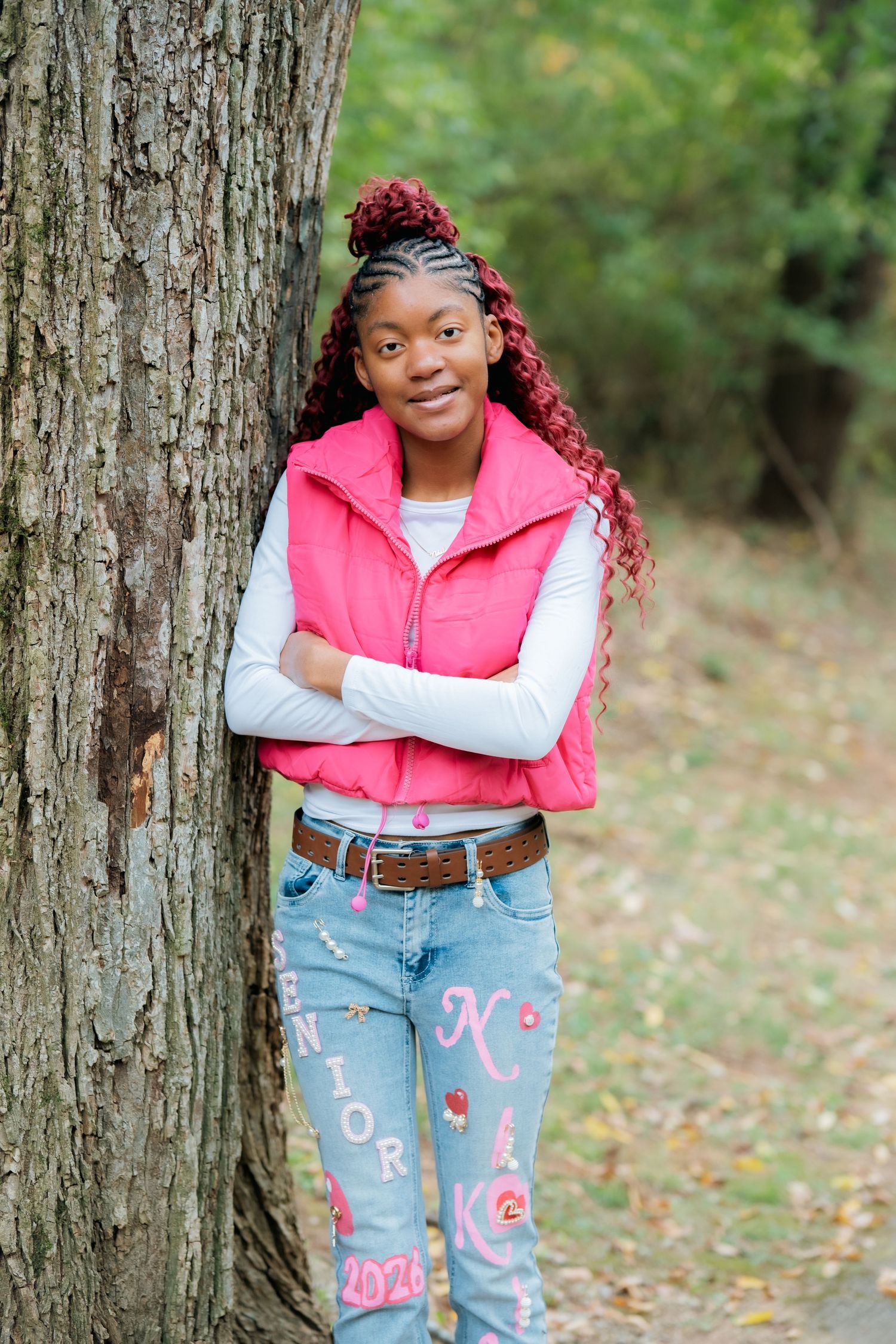 Casual outdoor portrait against tree trunk wearing pink vest and decorated denim.