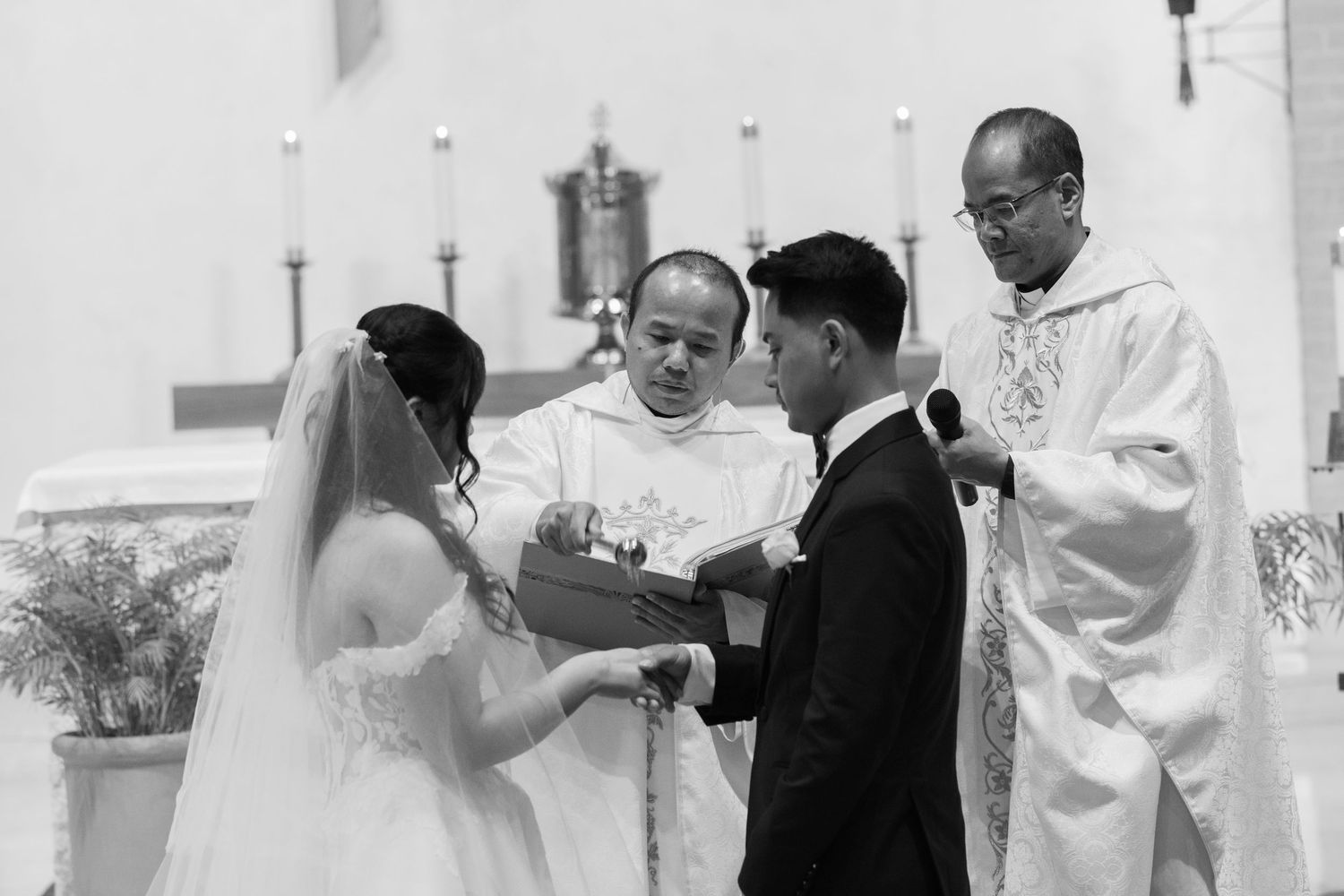 A wedding ceremony in progress at a bright church altar with white decor.