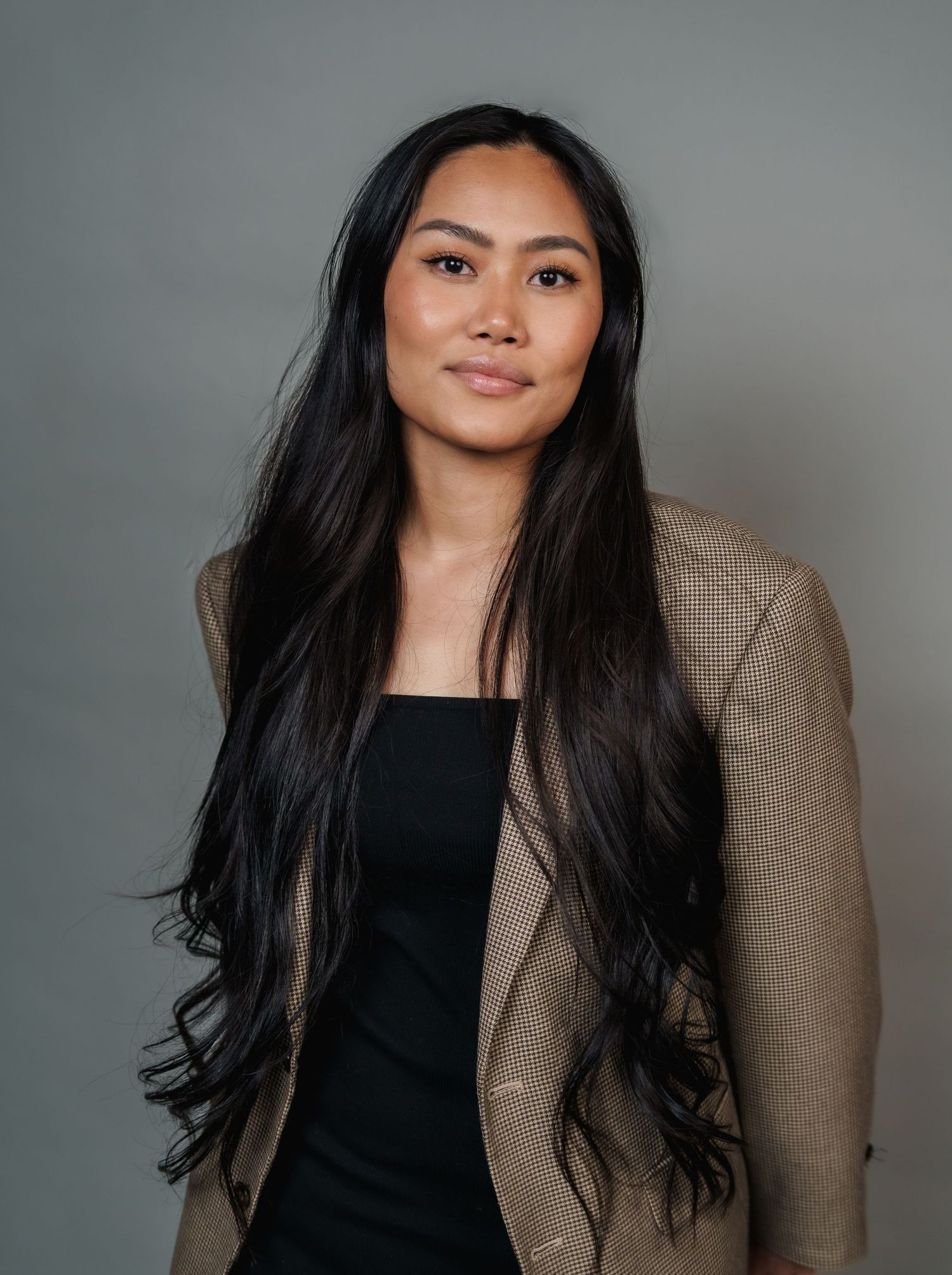 Professional studio portrait series showing a black blazer and flowing dark hair against a gray background.