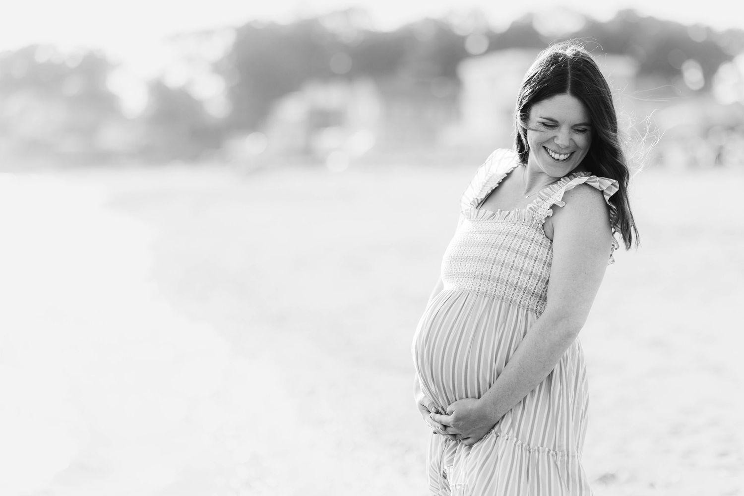 Pregnant woman cradling her belly during a Connecticut maternity session at the beach — Minmo Photography