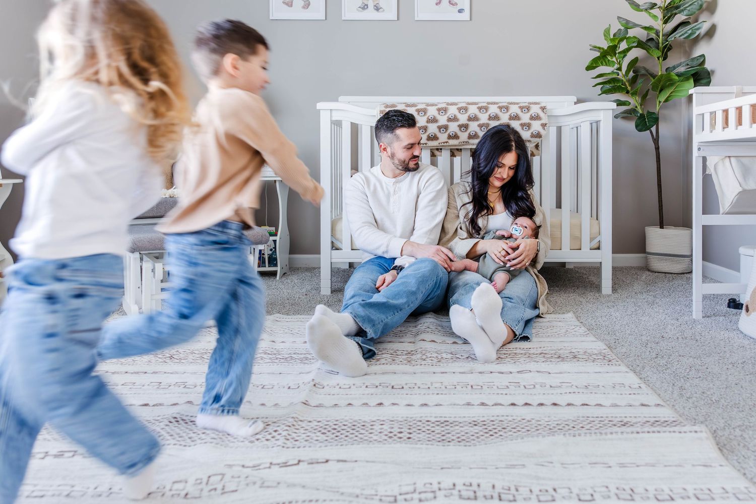Parents cradling their newborn during in-home newborn session in Connecticut while older siblings run around — Minmo Photography