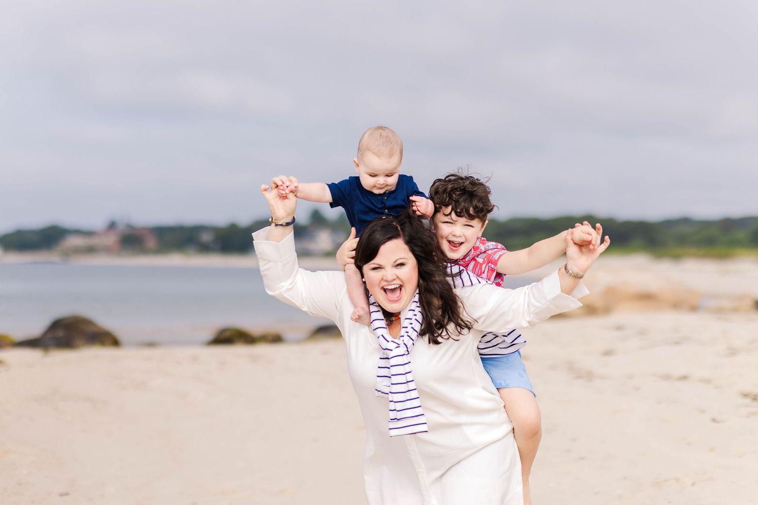 Mom holding two toddlers on her shoulders during photoshoot at a Connecticut beach — Minmo Photography