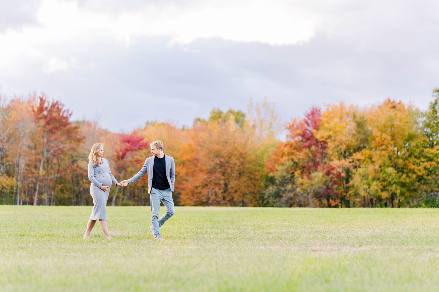 Wide shot of couple walking through a field during fall maternity session -- Minmo Photography