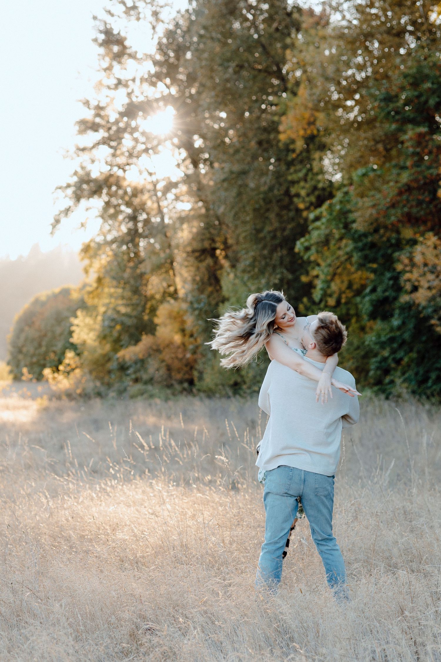 A couple embraces in a sun-drenched field with golden light streaming through trees during sunset in Boise Idaho