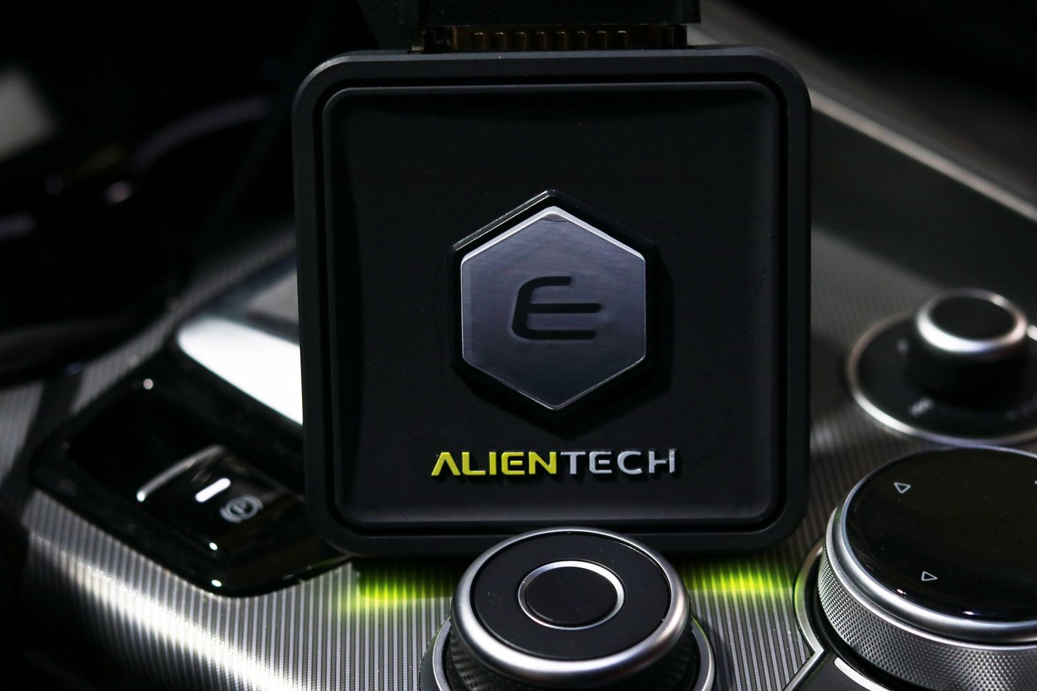 Close-up view of black gaming controller buttons with green LED lighting and Alientech branding.