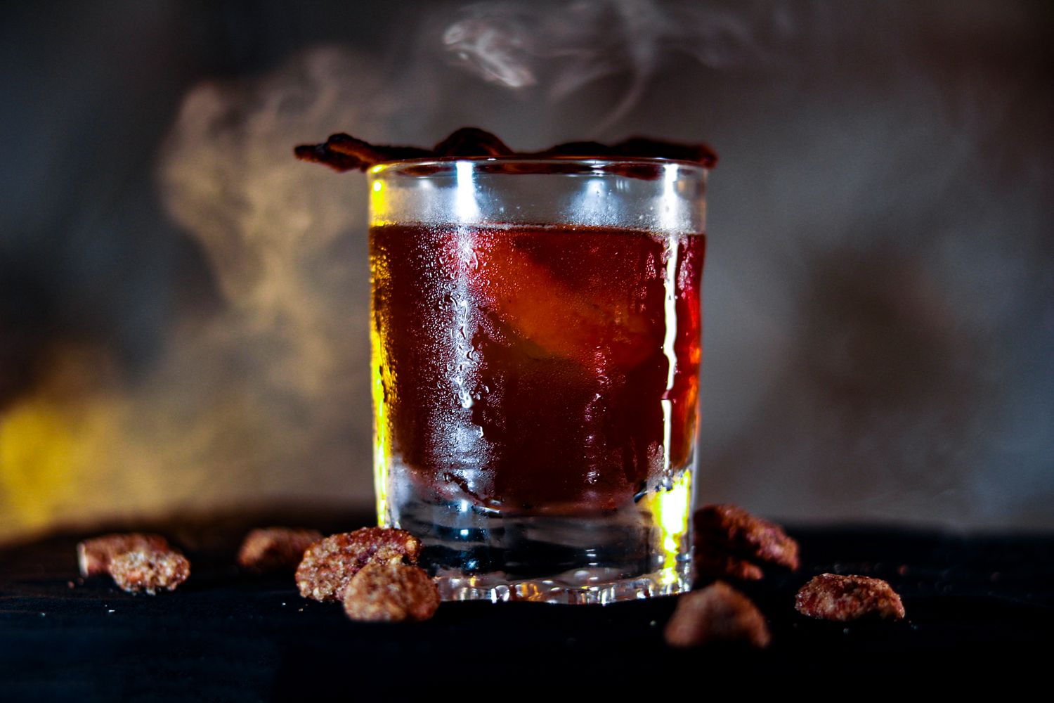 Close-up shot of an old fashioned cocktail  in a rocks glass with dark background and smoky atmosphere.