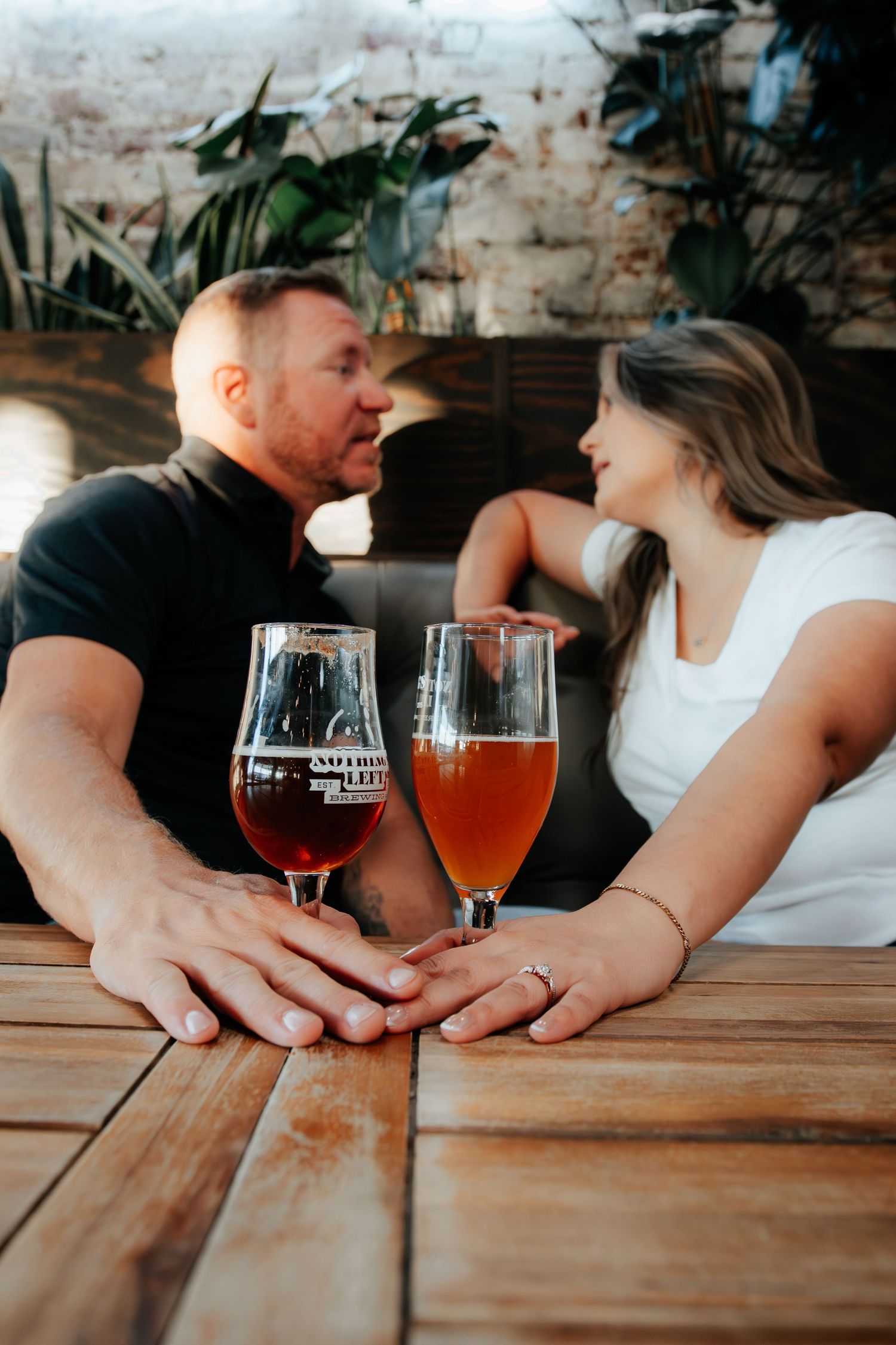 Couple holding hands at a wooden table with craft beer glasses, sharing a romantic moment at a brewery.