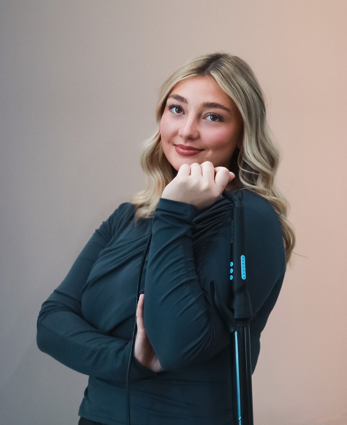 Professional headshots of a hairstylist in a dark sweater against neutral background.