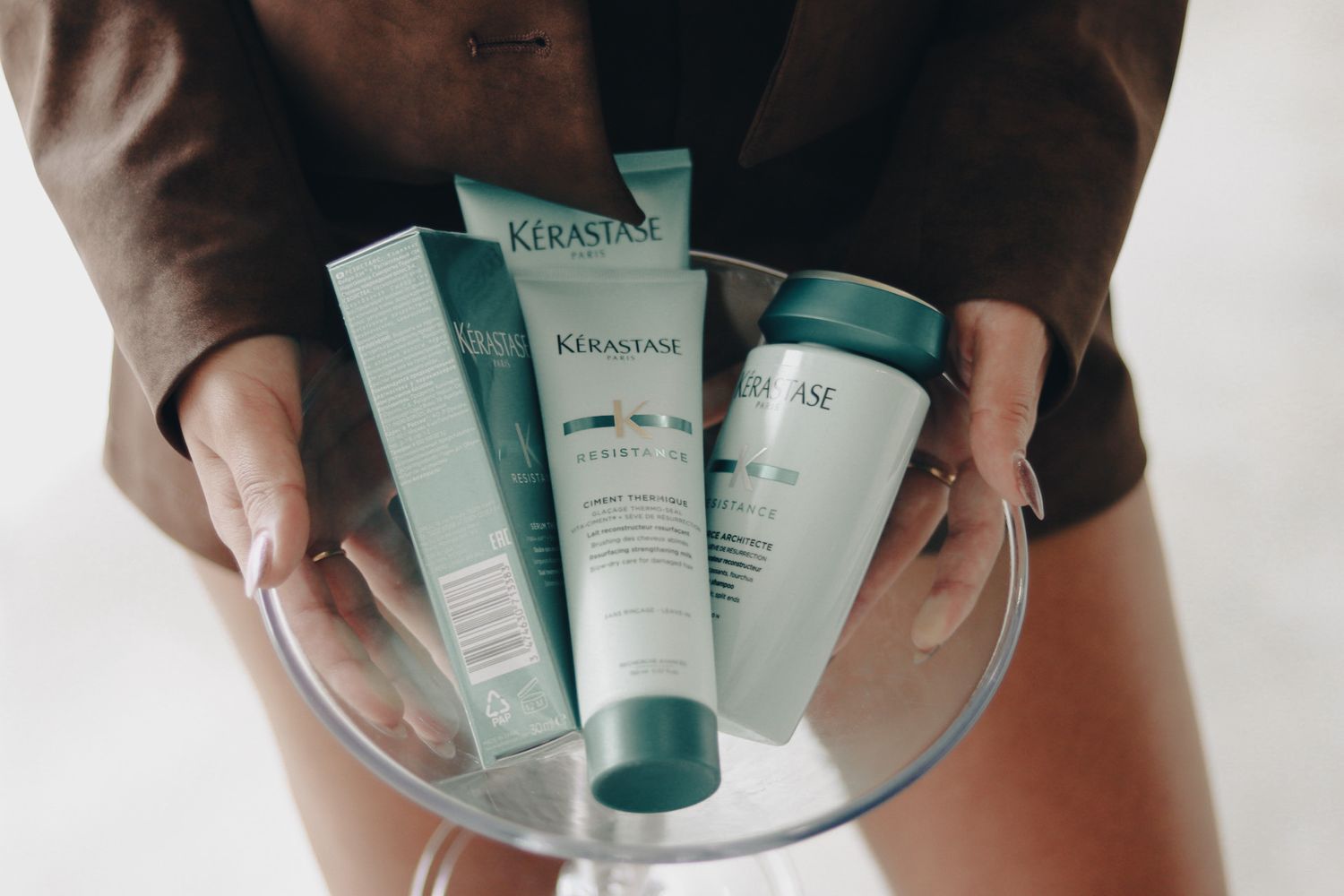 Hands demonstrating the application of skincare products from teal-colored tubes against a white background.
