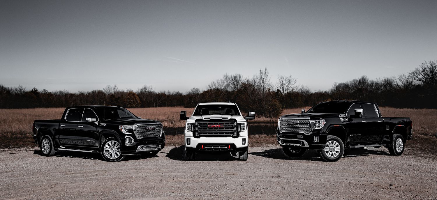 Three black GMC Sierra pickup trucks parked side by side on a dirt lot with bare trees in the background.