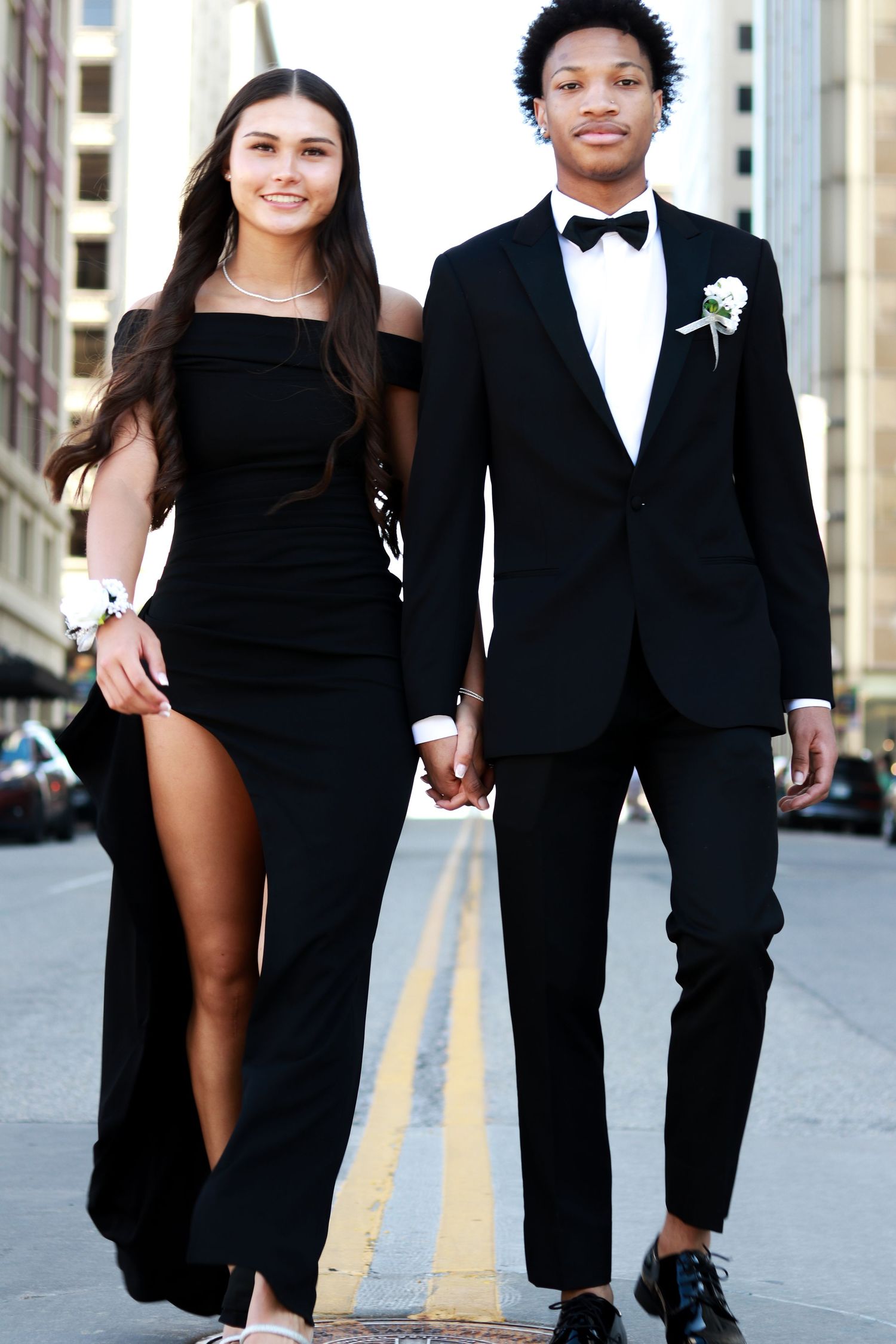 Stylish couple in black formal attire poses together on city street for romantic engagement photos.