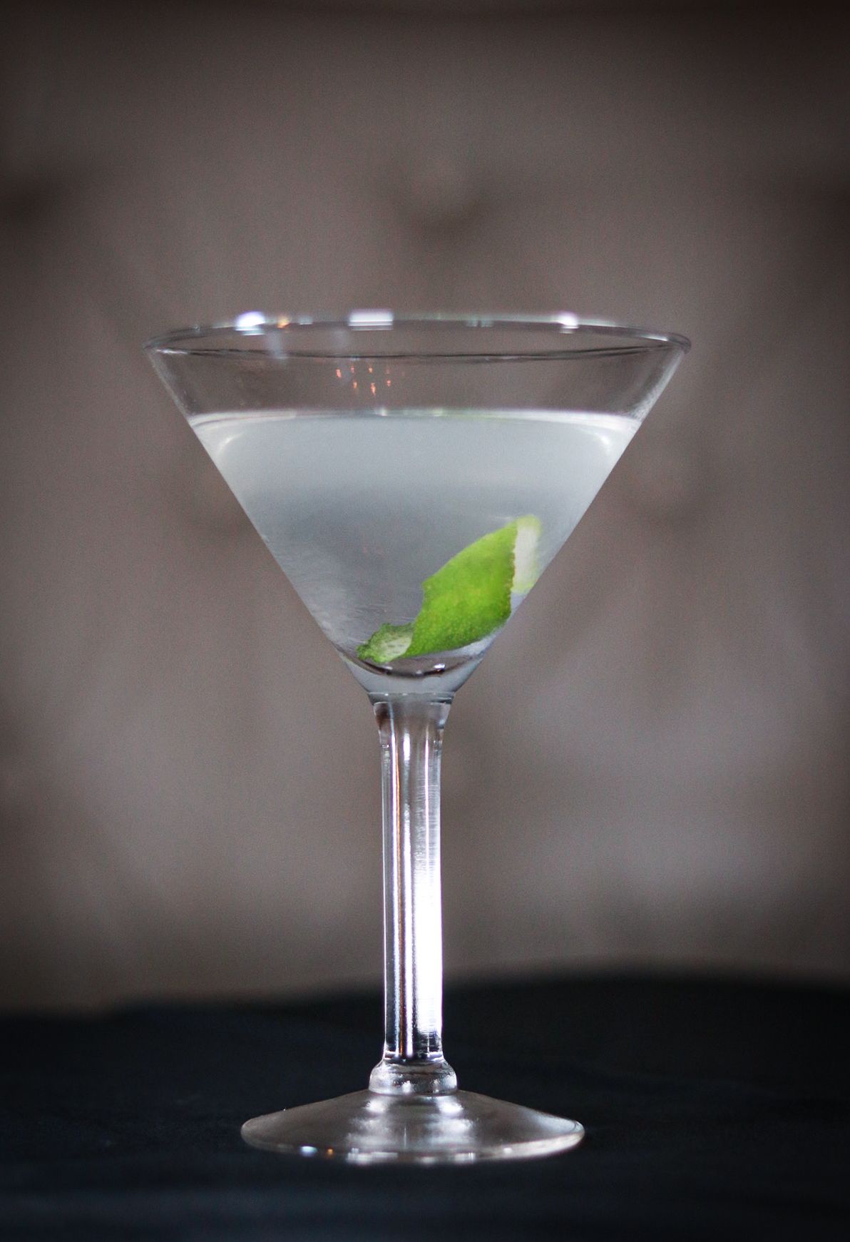 Elegant martini glasses with clear liquid and basil leaf garnish on dark backdrop.