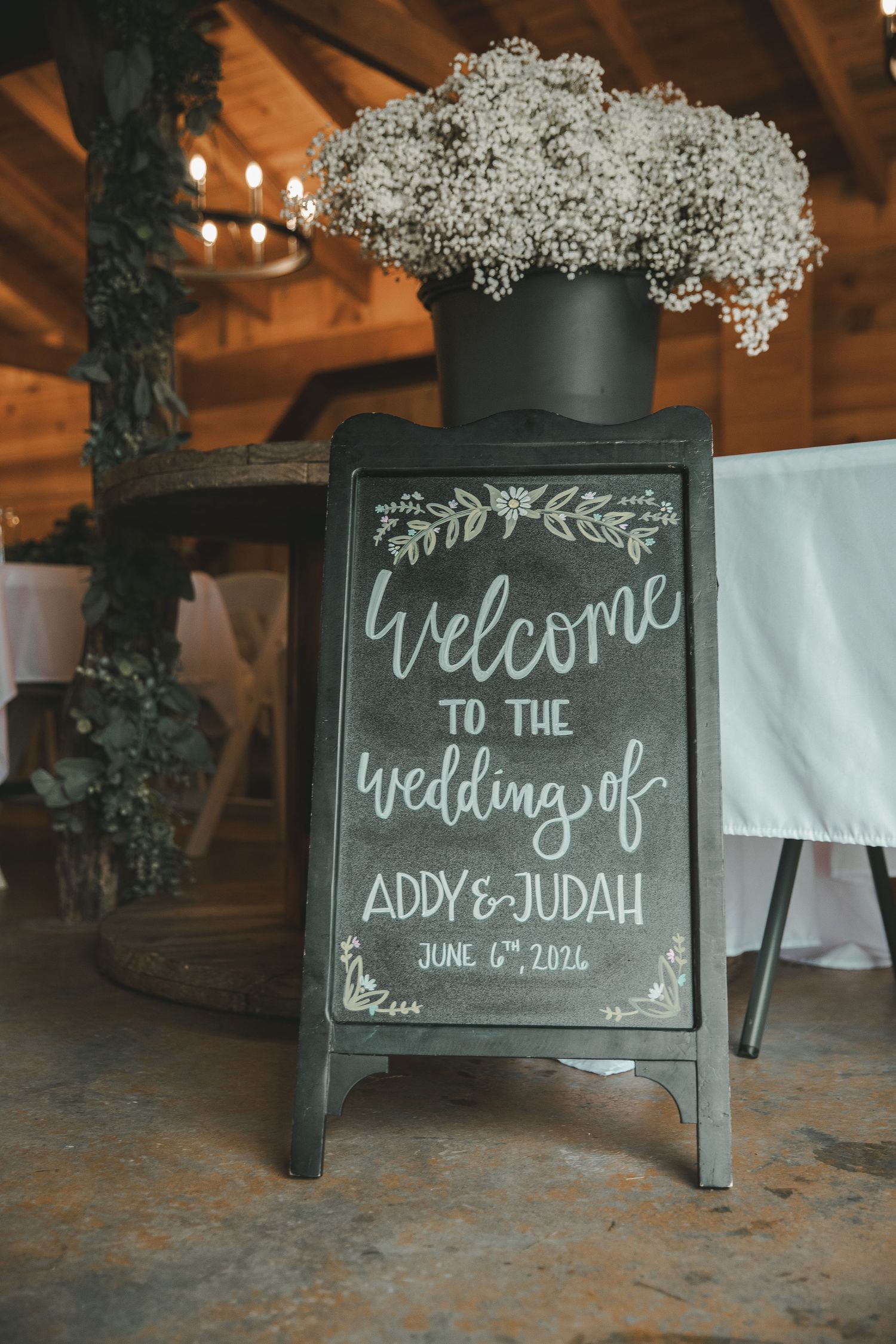 Rustic chalkboard wedding welcome sign for Addy and Judah, June 6th 2021, adorned with baby's breath flowers in a barn.