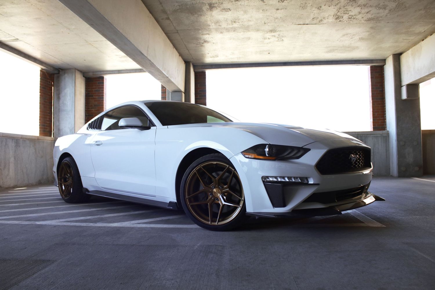 White Ford Mustang GT with black wheels parked in a concrete garage, showcasing its sleek fastback design.