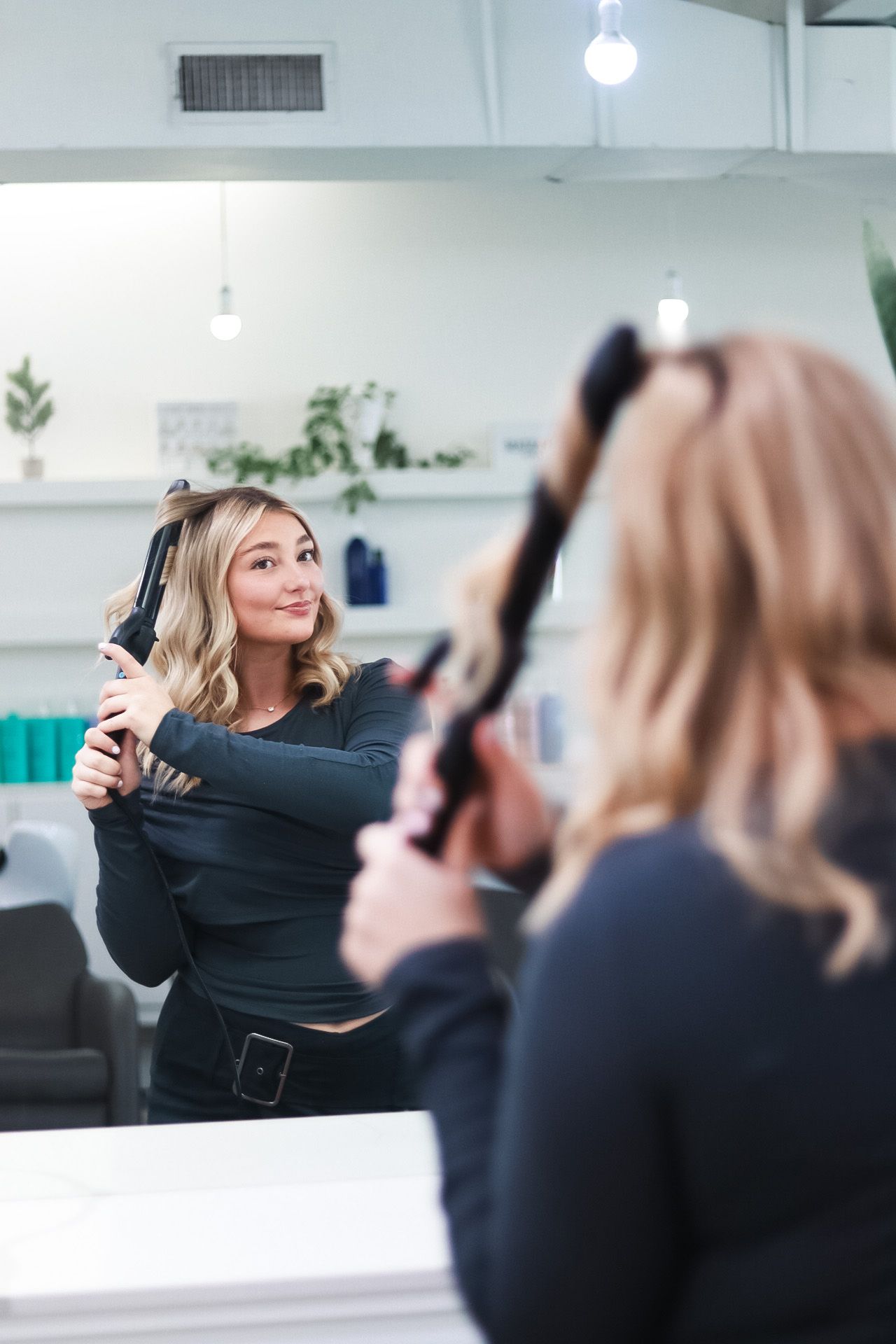 Professional headshots of a hairstylist posing in front of mirror curling her hair.