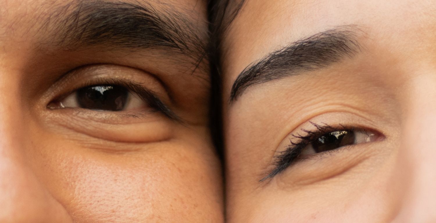 Close-up of two people's eyes side by side, showcasing diverse skin tones and eye shapes in an intimate portrait.