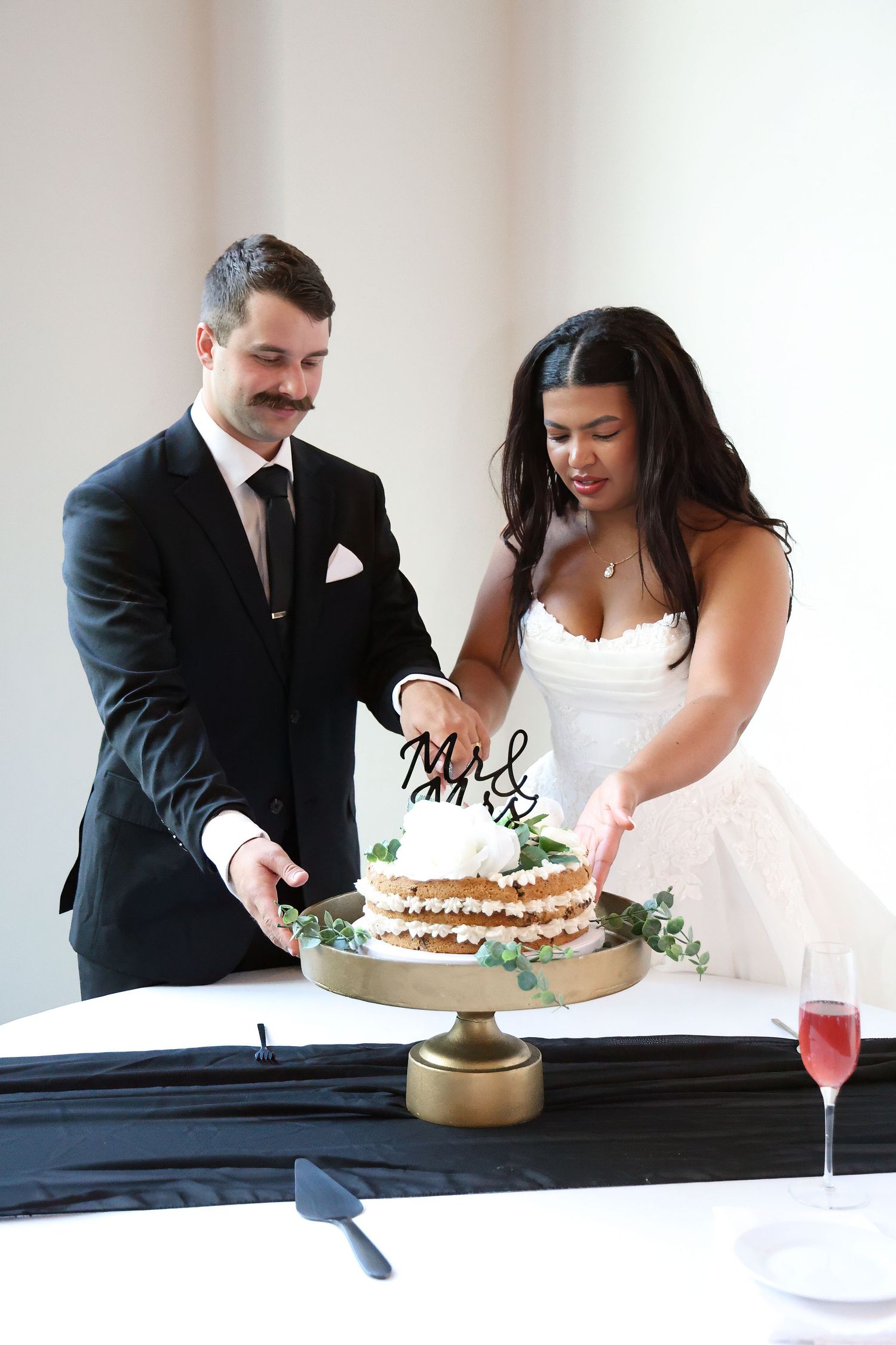 Bride and groom cutting their wedding cake together, decorated with Mr & Mrs topper and greenery.