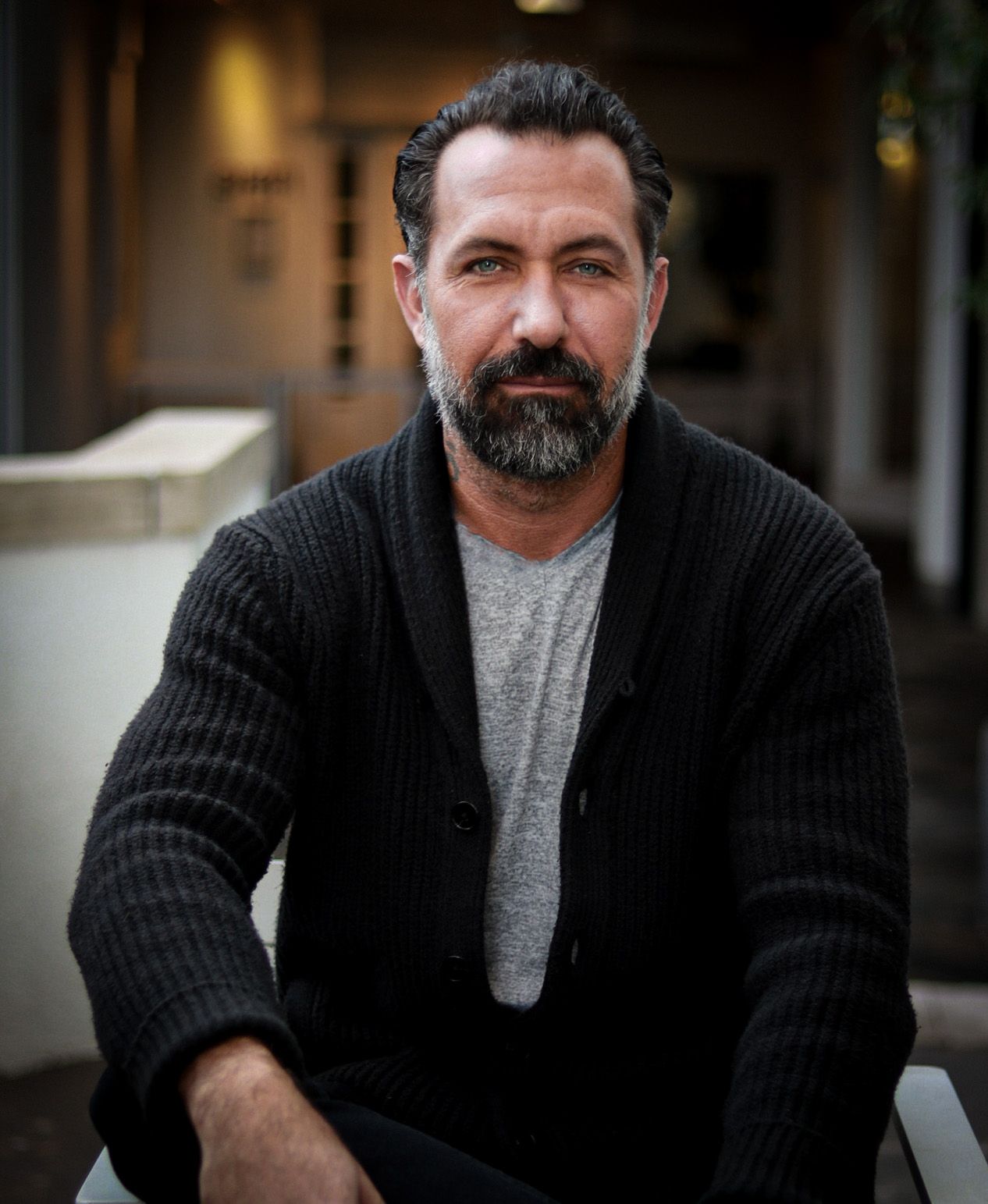 Person in black knit sweater sitting against dark background.
