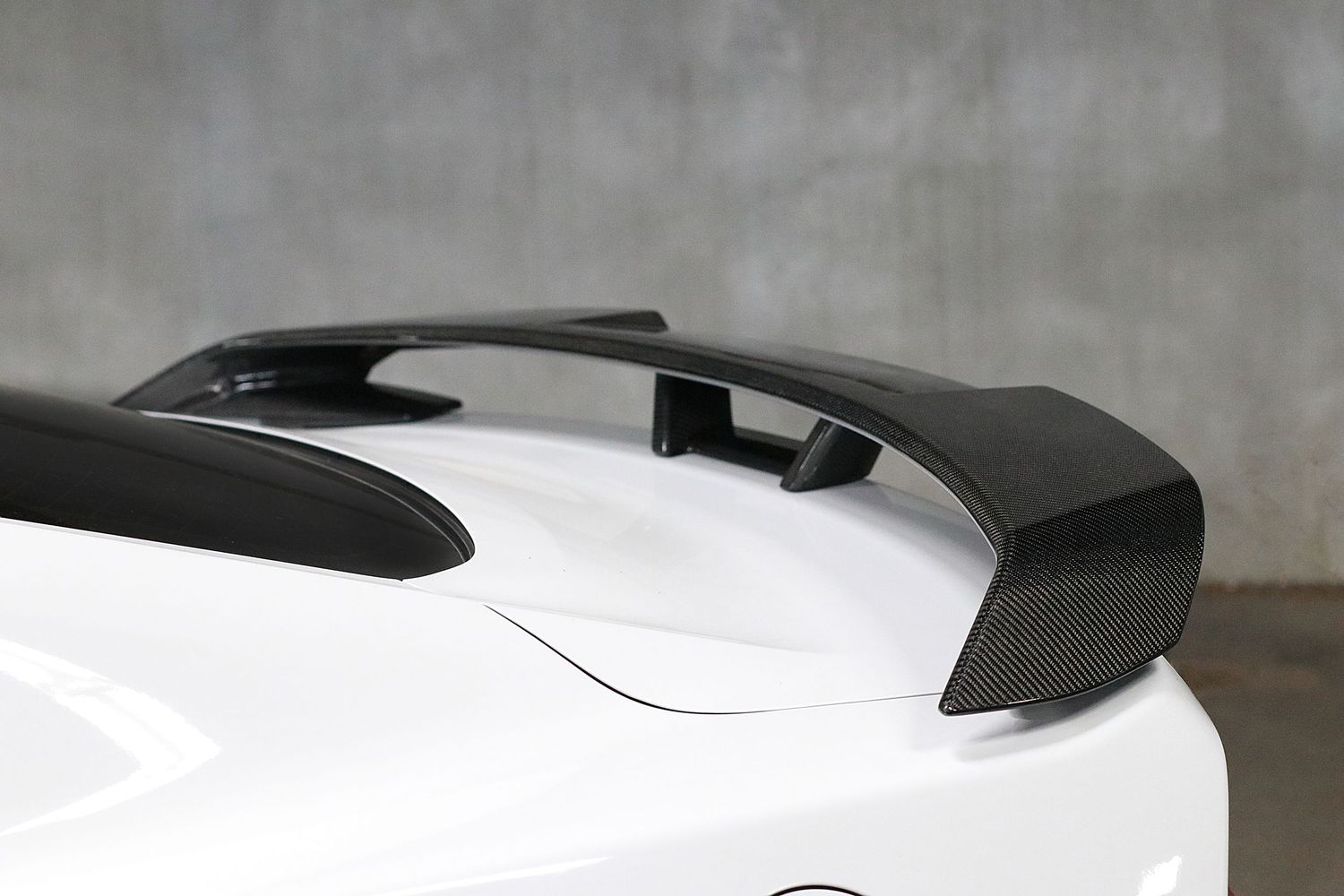 Carbon fiber GT rear spoiler wing on a white sports car, aerodynamic performance upgrade for enhanced downforce.