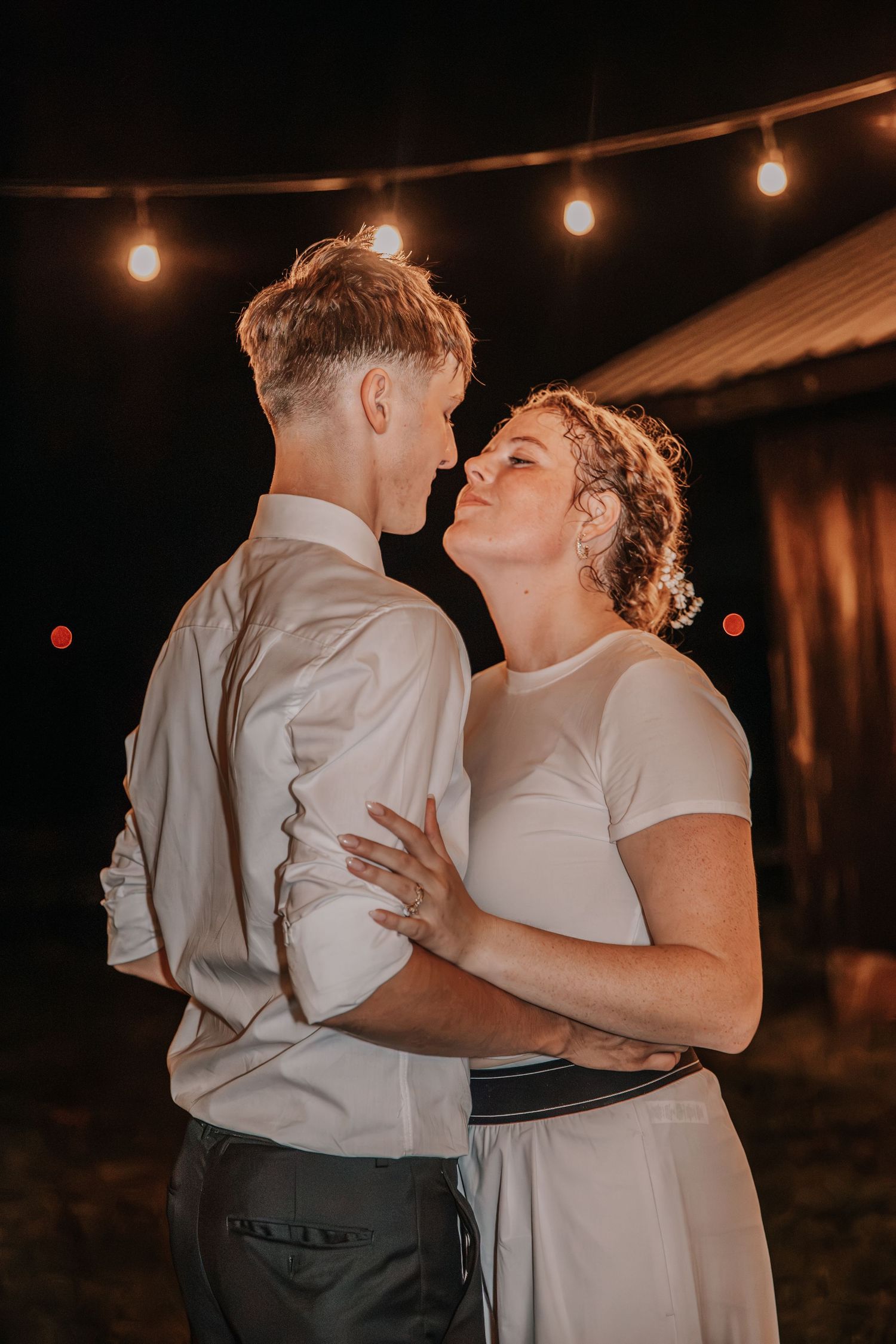 Couple sharing a romantic first dance outdoors at night under warm string lights at a wedding reception.