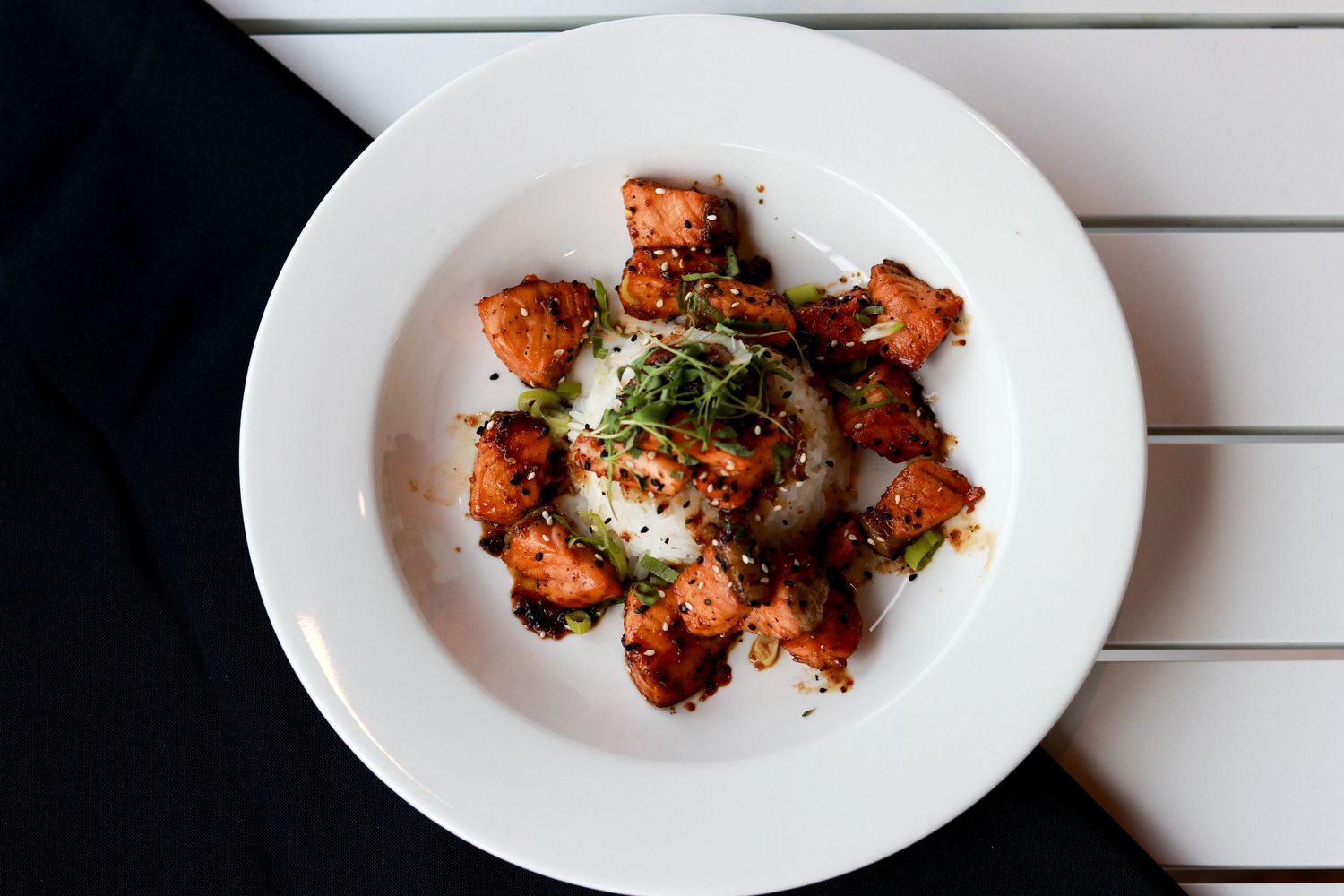 Crispy glazed chicken wings arranged in a circle on a white plate with herbs and sauce on a wooden surface.