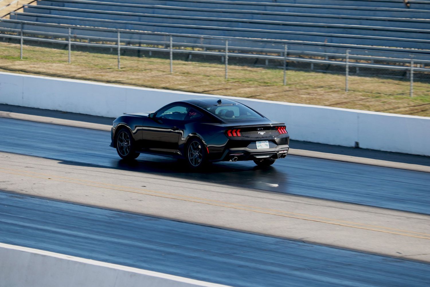 Black Ford Mustang racing on a drag strip track at a motorsport facility on a sunny day.