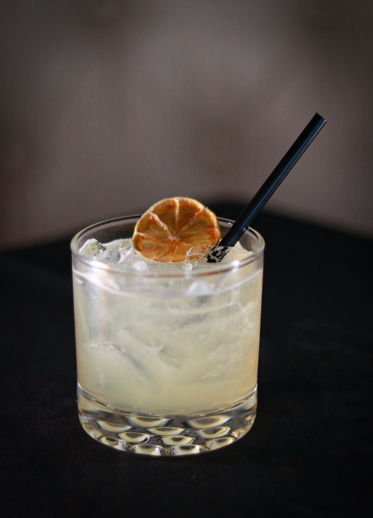 Citrus cocktail with ice and orange garnish in rocks glass with black straw.