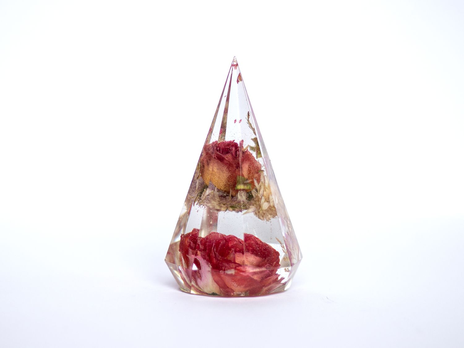 Clear resin pyramid paperweight with preserved red roses and dried flowers encased inside, on white background.