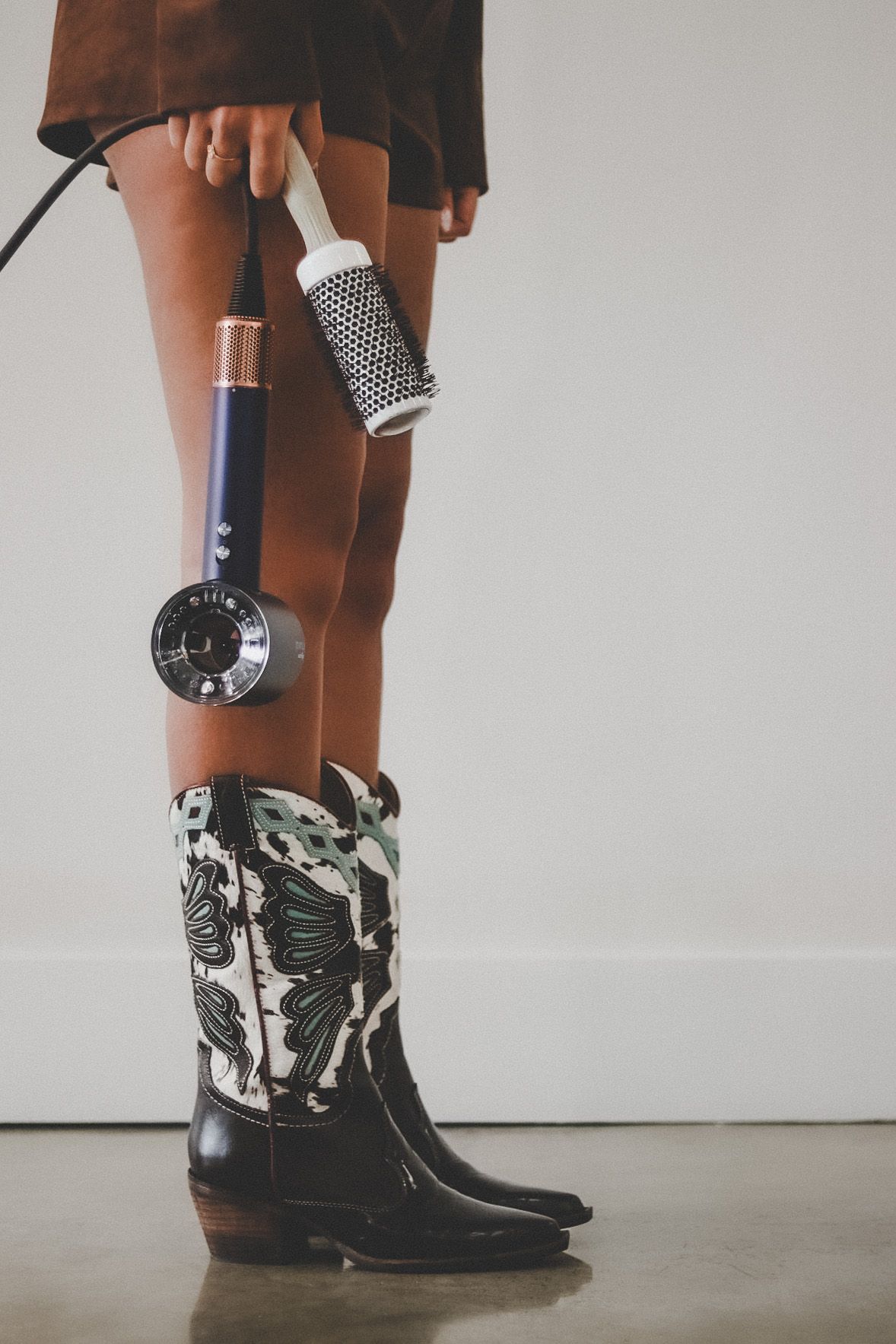 Black and white cowboy boots with patterned details shown from different angles against a white wall background.