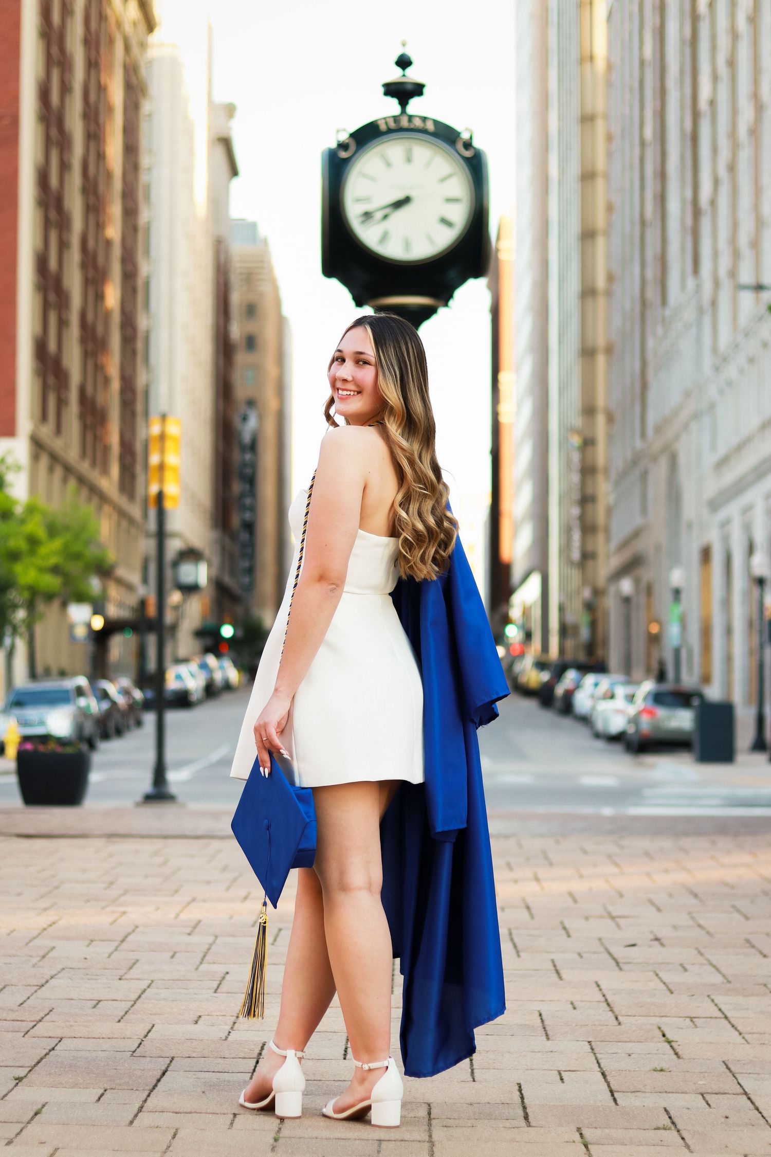 Stylish graduation photo series showing close-up details of white dress and blue cap and gown against urban backdrop.