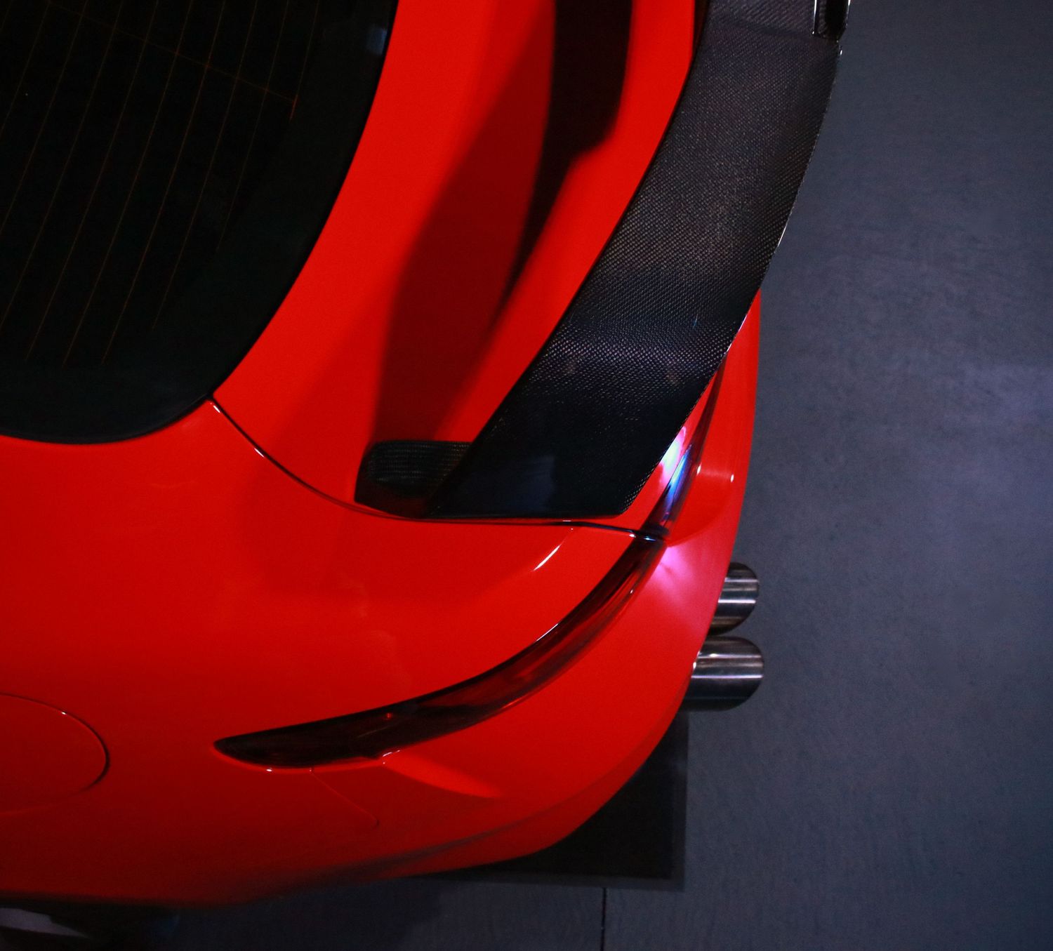 Close-up detail shot of a bright red sports car body panel in dramatic lighting.