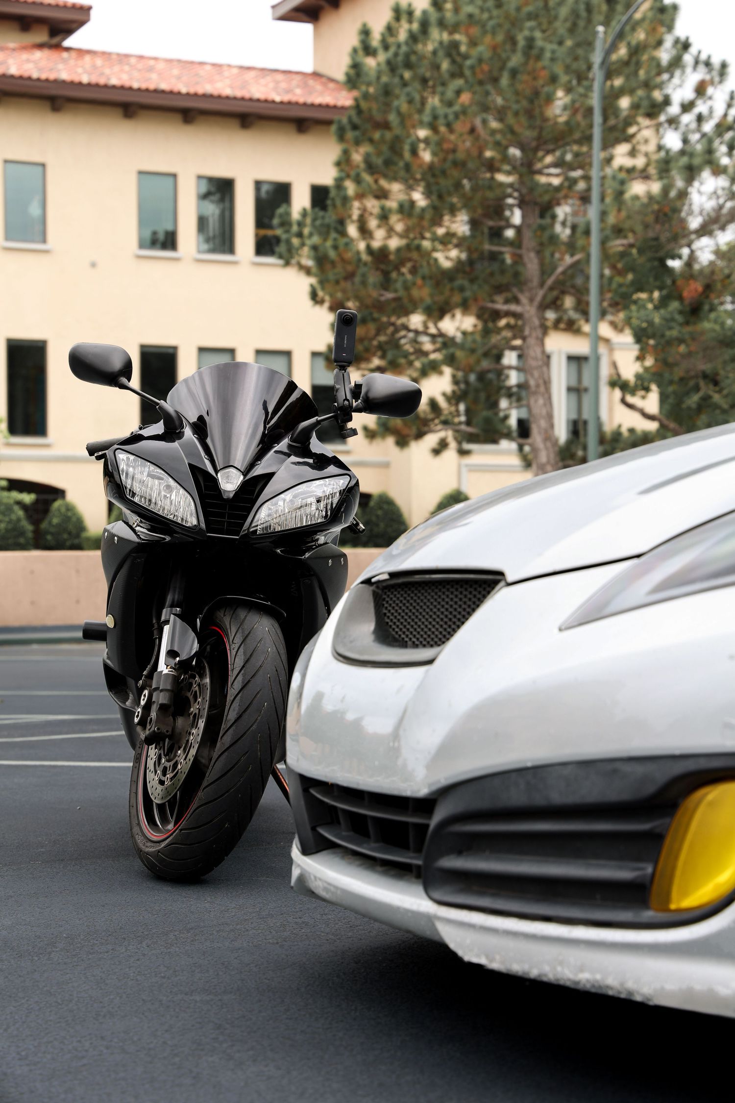 A sleek black sport motorcycle parked next to a white car in a parking lot with a beige building in the background.